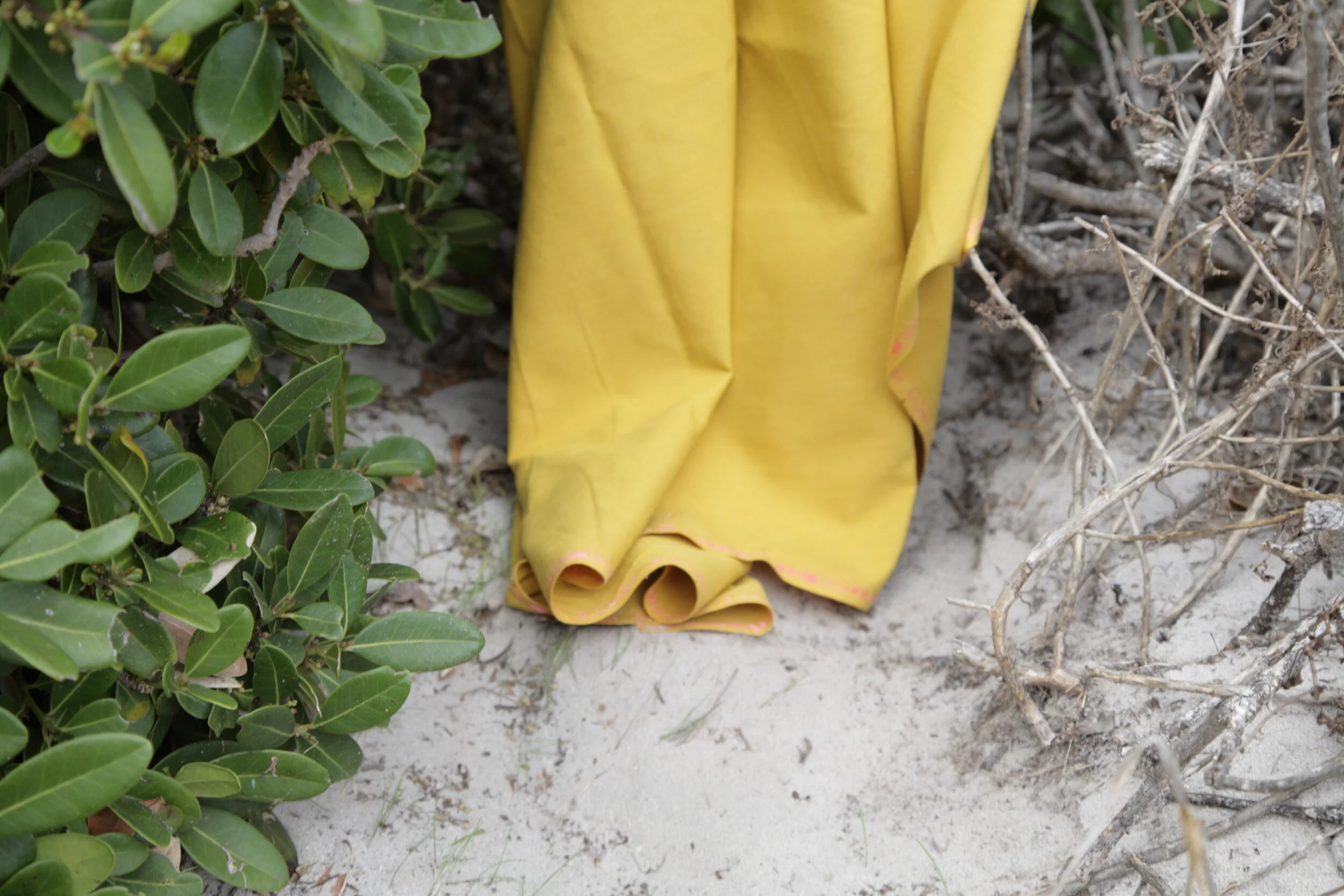 Yellow raincoat draped over sand and surrounded by green bushes and dry, bare branches.