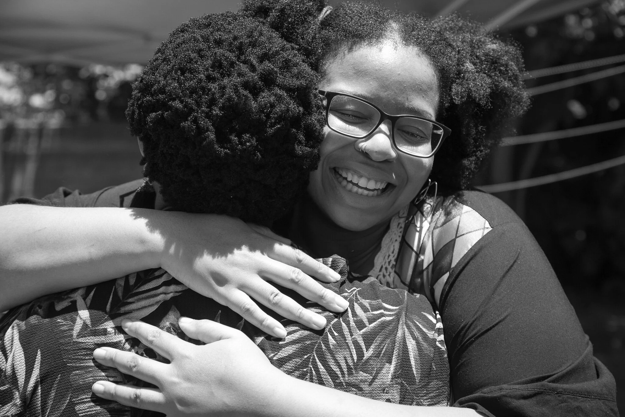 Two women hugging, one with short dark curly hair and glasses, smiling broadly.