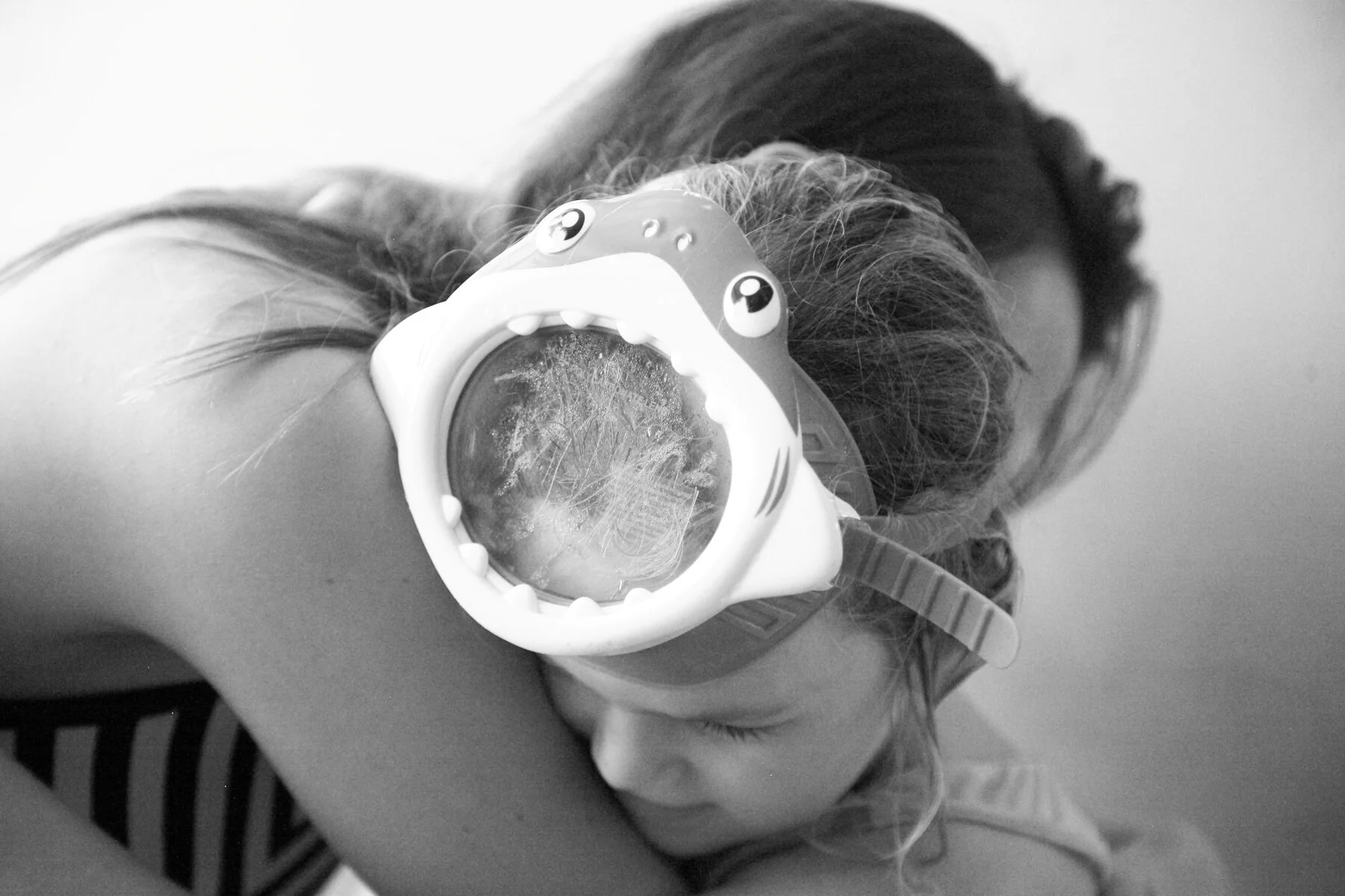 A young girl hugging an adult with her head resting on the person's shoulder, wearing goggles with a clownfish design.