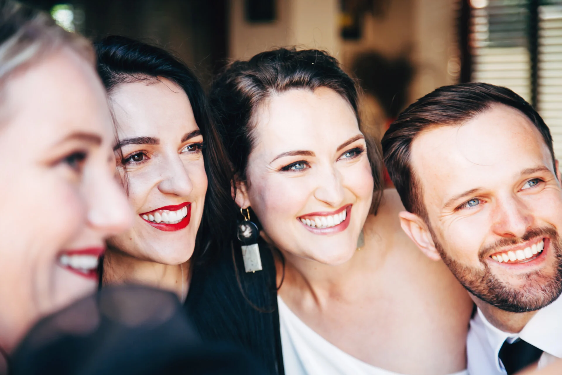 Four cheerful people smiling and taking a photo together at a social event, dressed in elegant attire.