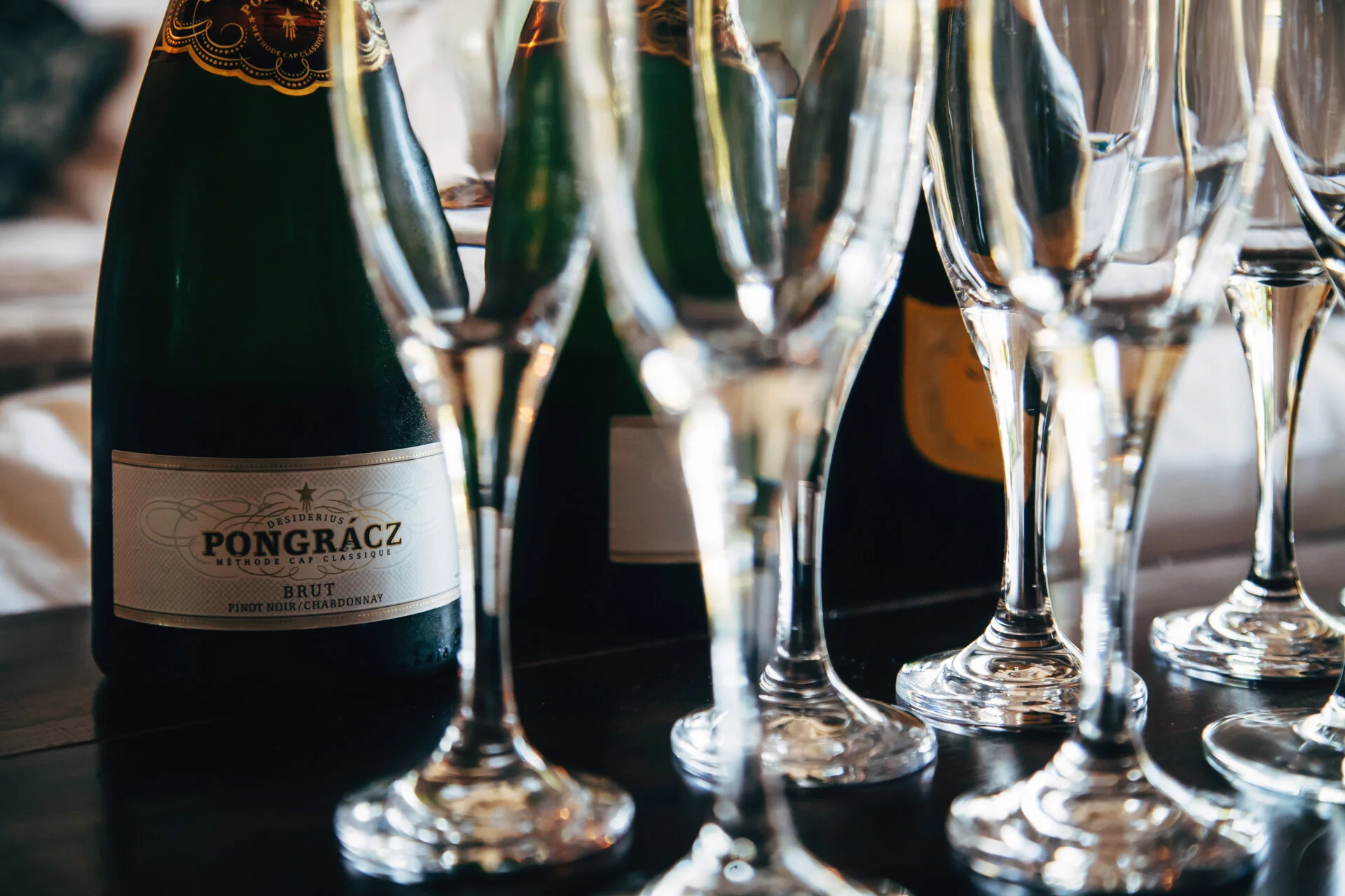 Close-up of a champagne bottle and multiple champagne flutes on a table, with reflections and a blurred background.