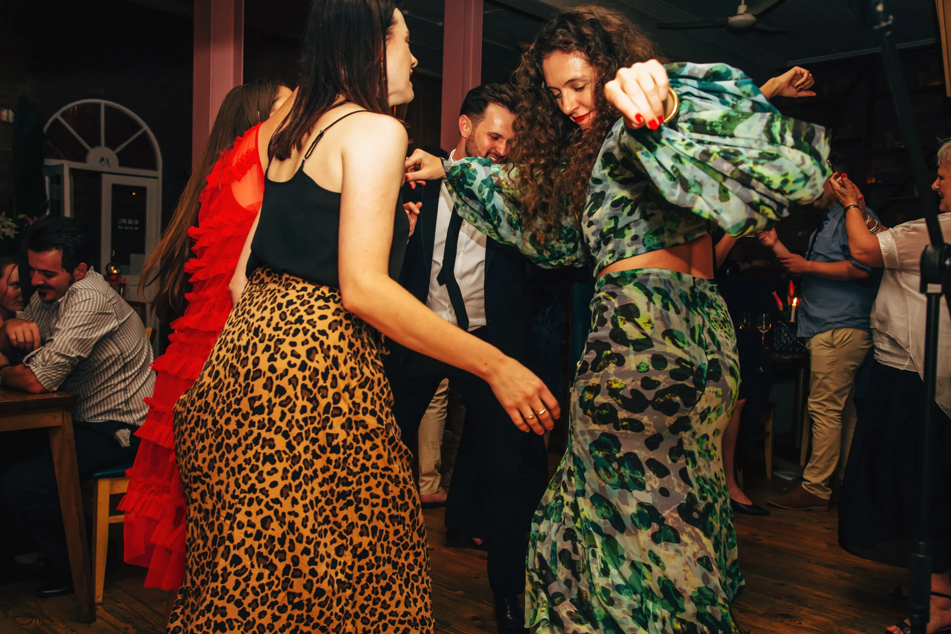 Wedding guests dancing together at a party, dressed in colorful outfits with animal print patterns, enjoying themselves in a lively social setting.
