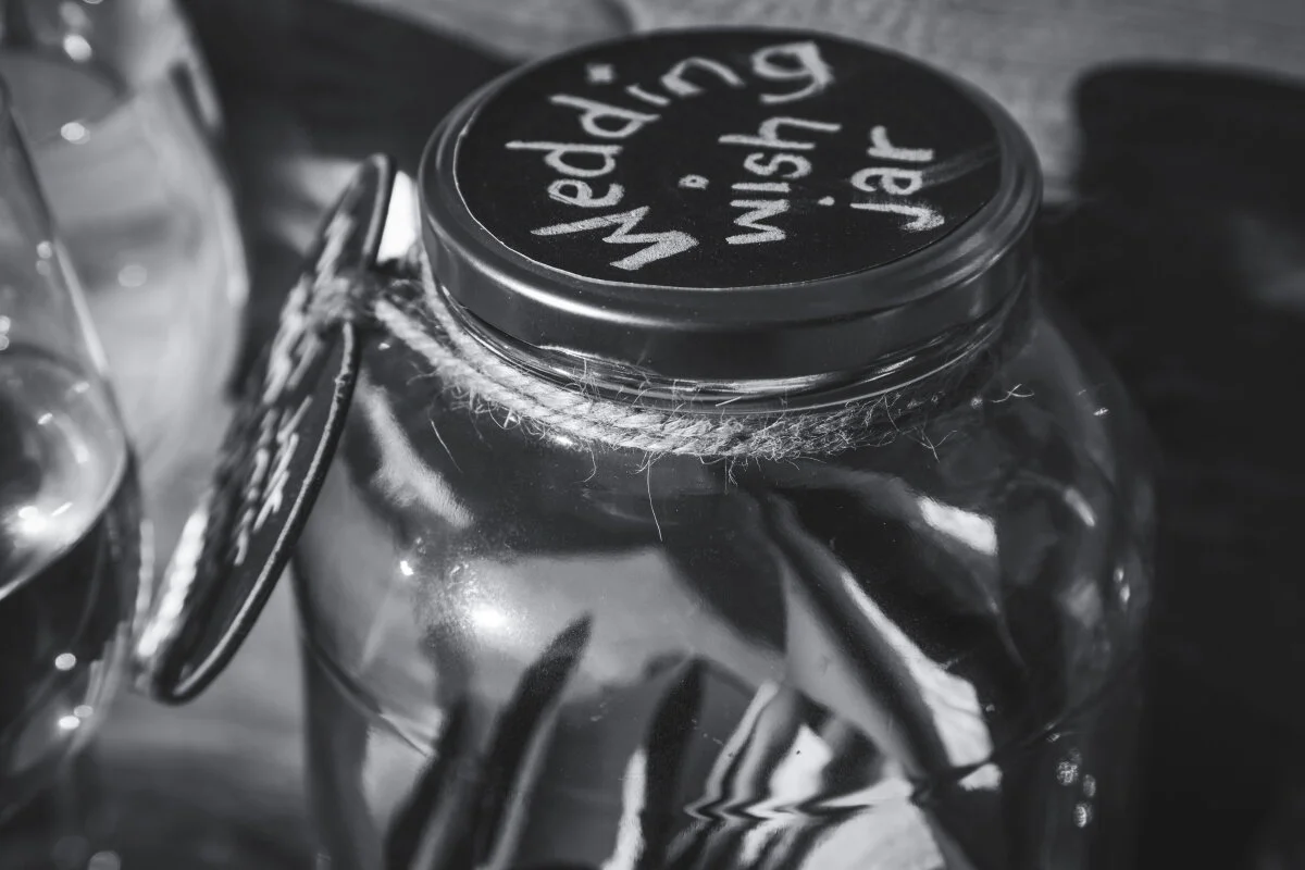 A glass jar with a black lid that has writing on it, and a label attached to the jar's side. The image is in black and white.