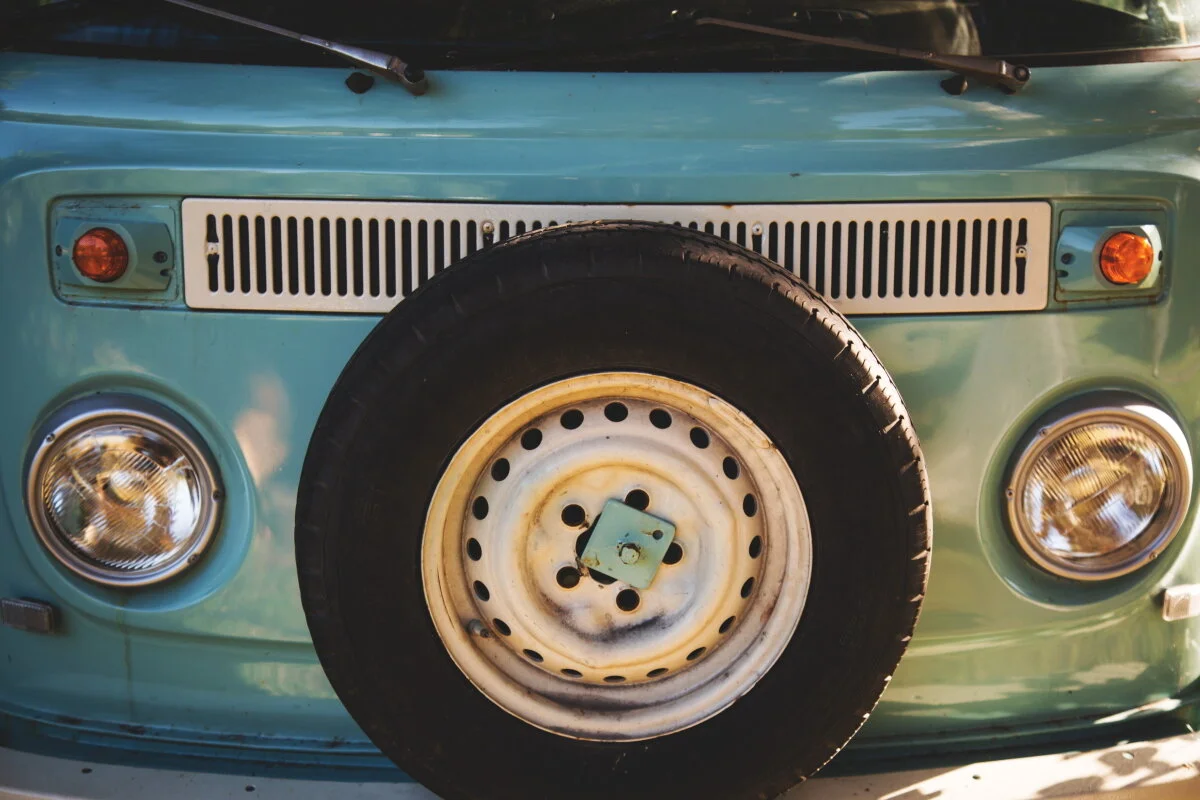 Front view of a vintage turquoise van with a spare tire mounted on the front.