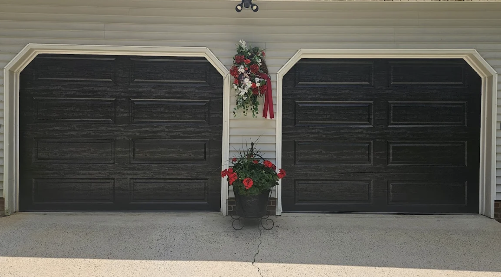Black double garage doors with floral decorations, including a bouquet of flowers above and a pot of red flowers in front.