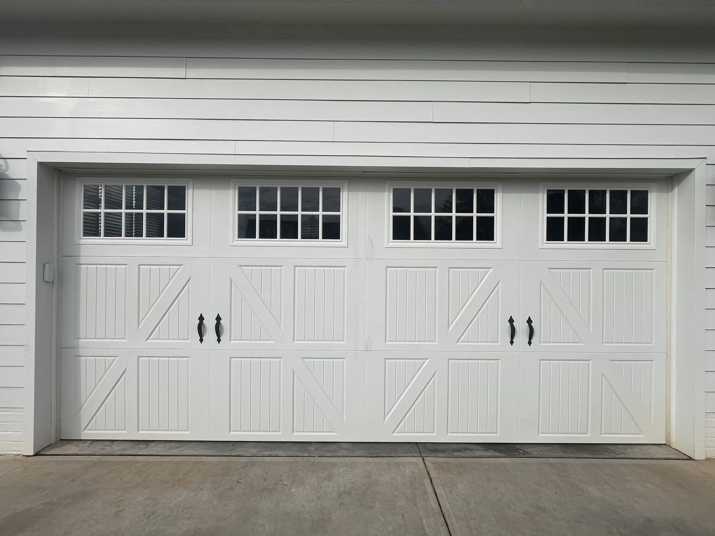 White garage door with four small windows along the top and black handles in the center.