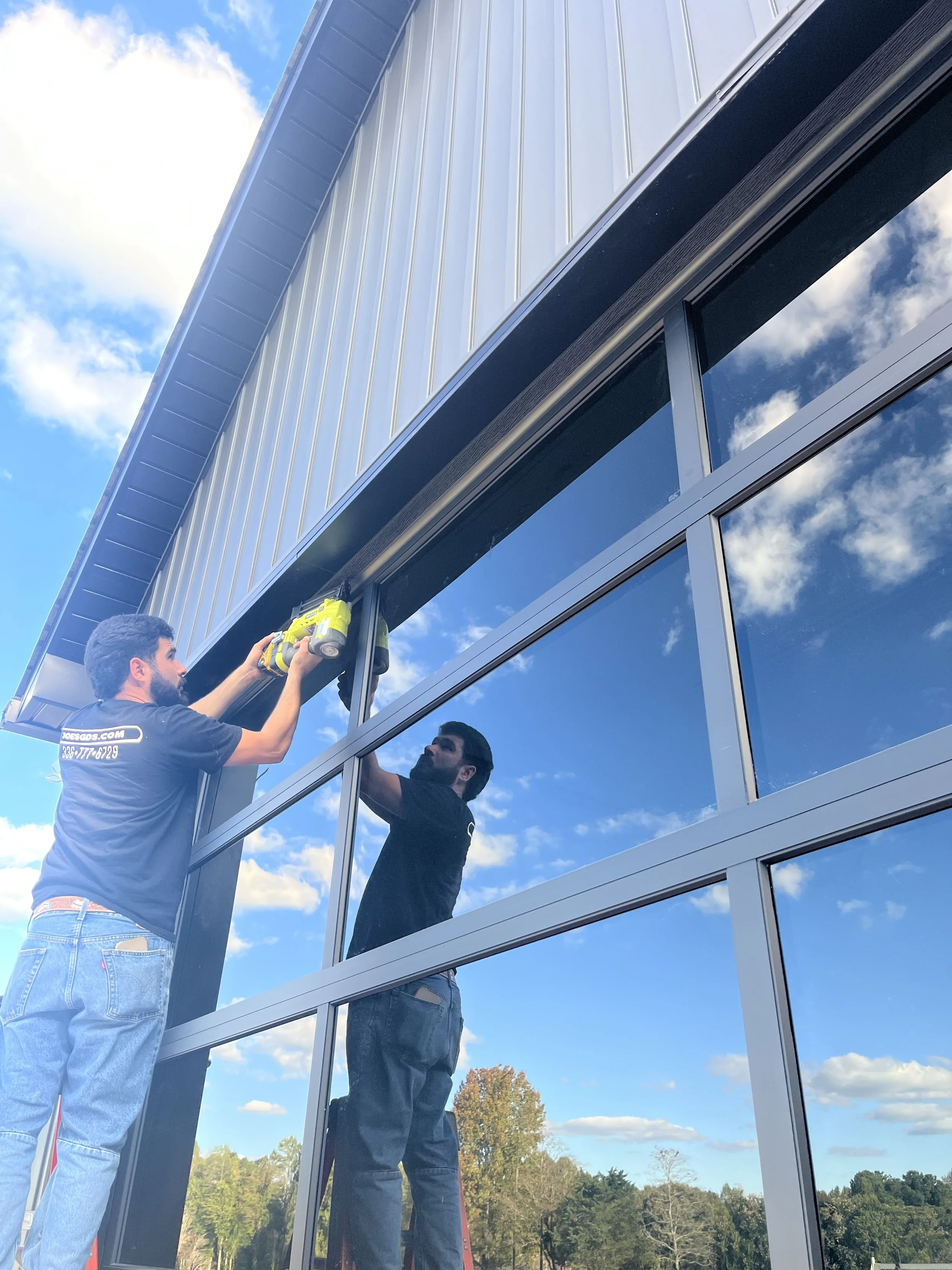 One worker installing or repairing glass windows on a building, using tools, with a blue sky and clouds reflected in the windows.