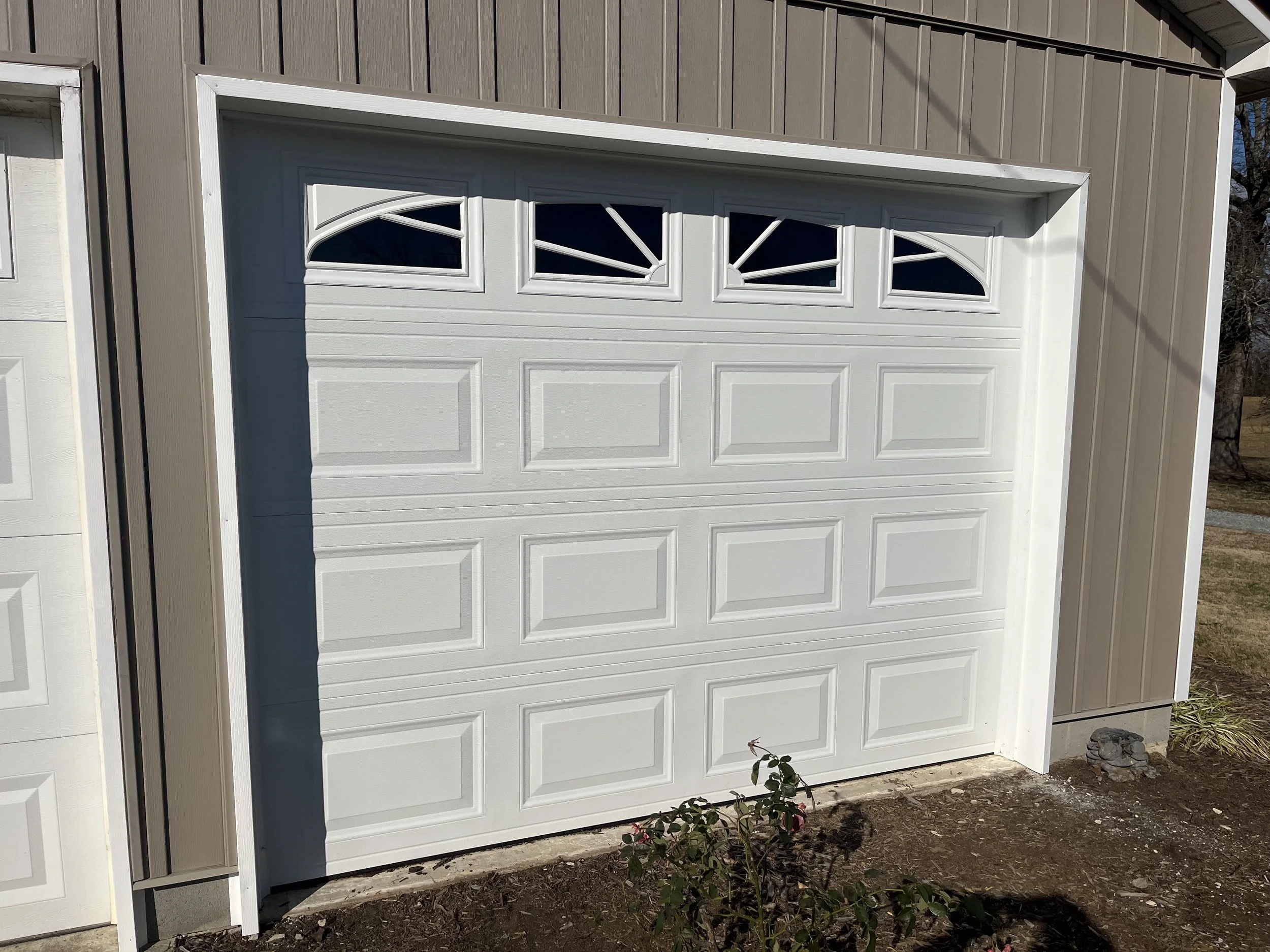 White garage door with five small arched windows at the top, installed in a beige building exterior with vertical siding.