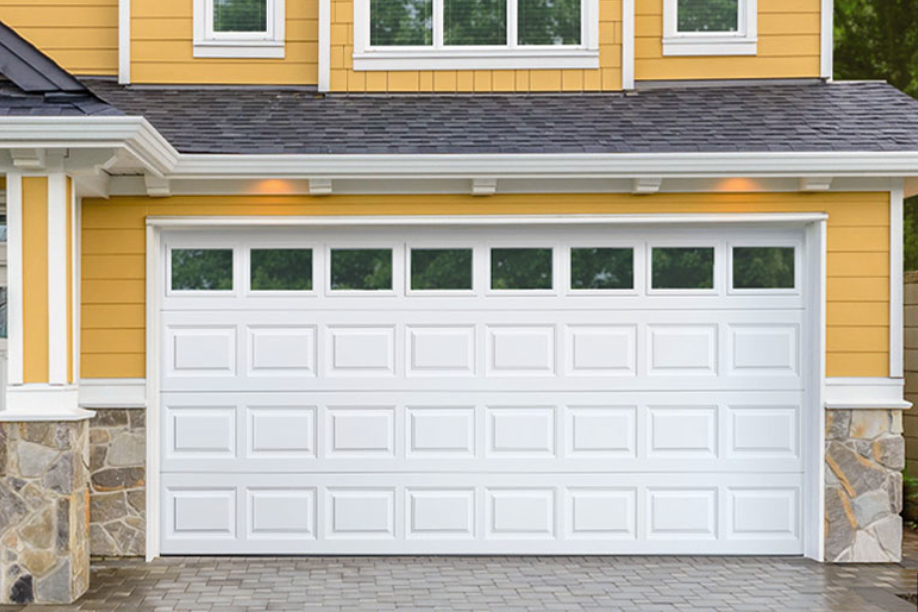 Front view of a yellow house with a white garage door and stone accents, with small windows above the garage.