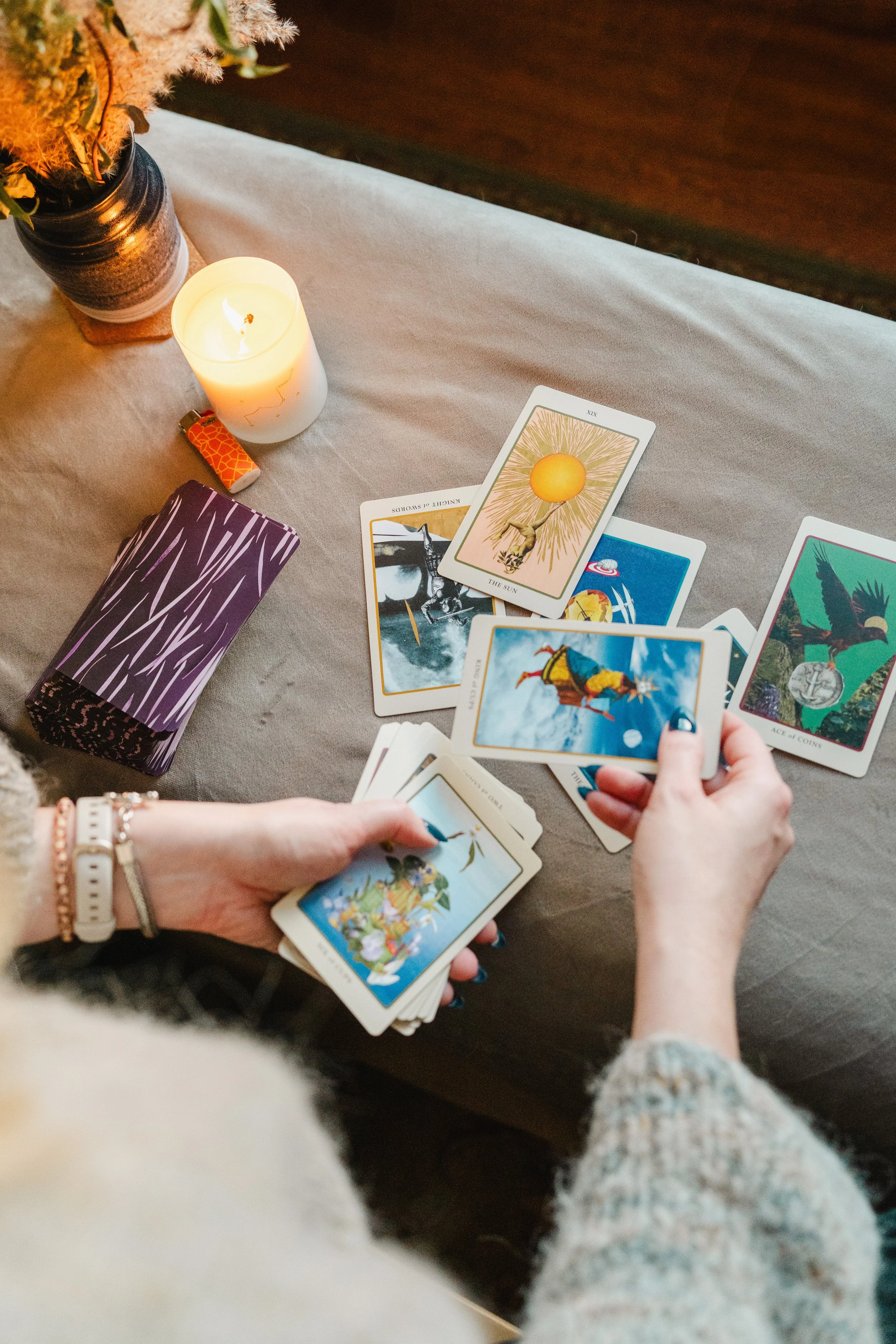Hands shuffling tarot cards with a lit candle and vase