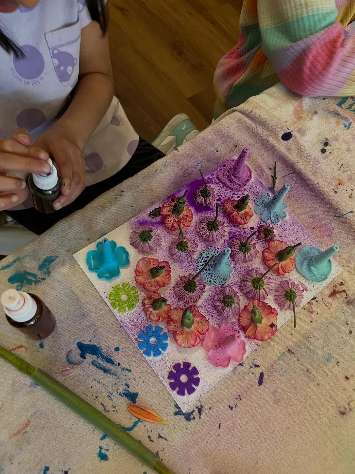Watercolor spray art with the Afternoon Art Explorers! Children arranged real flowers and plastic manipulatives on their papers and then sprayed with liquid watercolors. Then, they picked up the objects to reveal the white space left behind. They tur