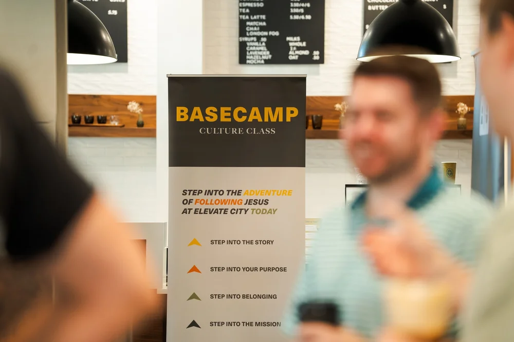 A Basecamp Culture Class banner beside the coffee bar, listing step into the story, your purpose, belonging and the mission