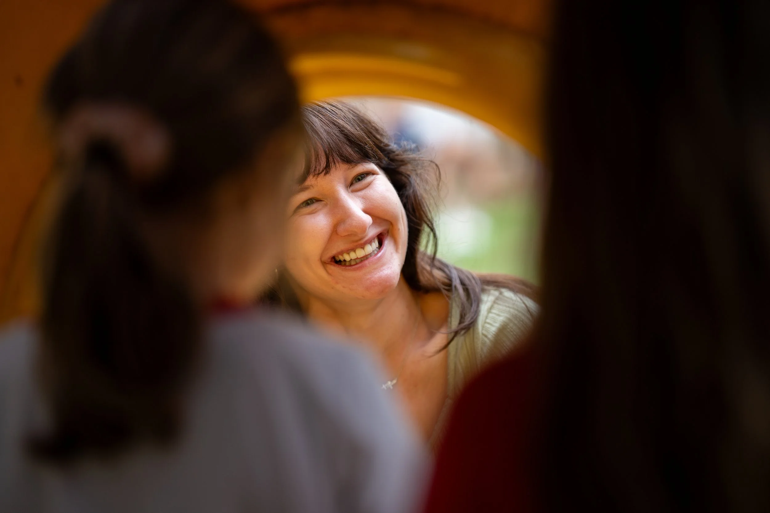 A woman laughing in the middle of a conversation, seen between two people in the foreground whose backs are to the camera.