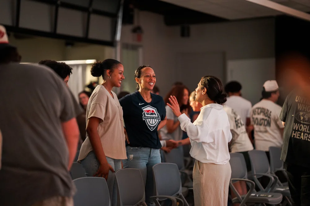 Three women standing together talking and laughing between the rows of chairs after a service at Peachtree Corners