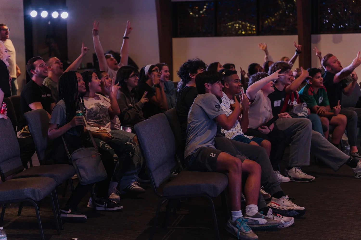 A packed room of middle and high schoolers at WAKE, hands in the air and laughing, leaders sitting among them