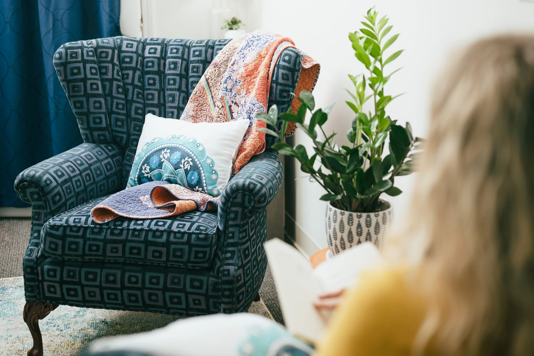 Comfy blue wingback chair with colorful throw blanket and pillow, awaiting clients in the Jen Carter Coaching office