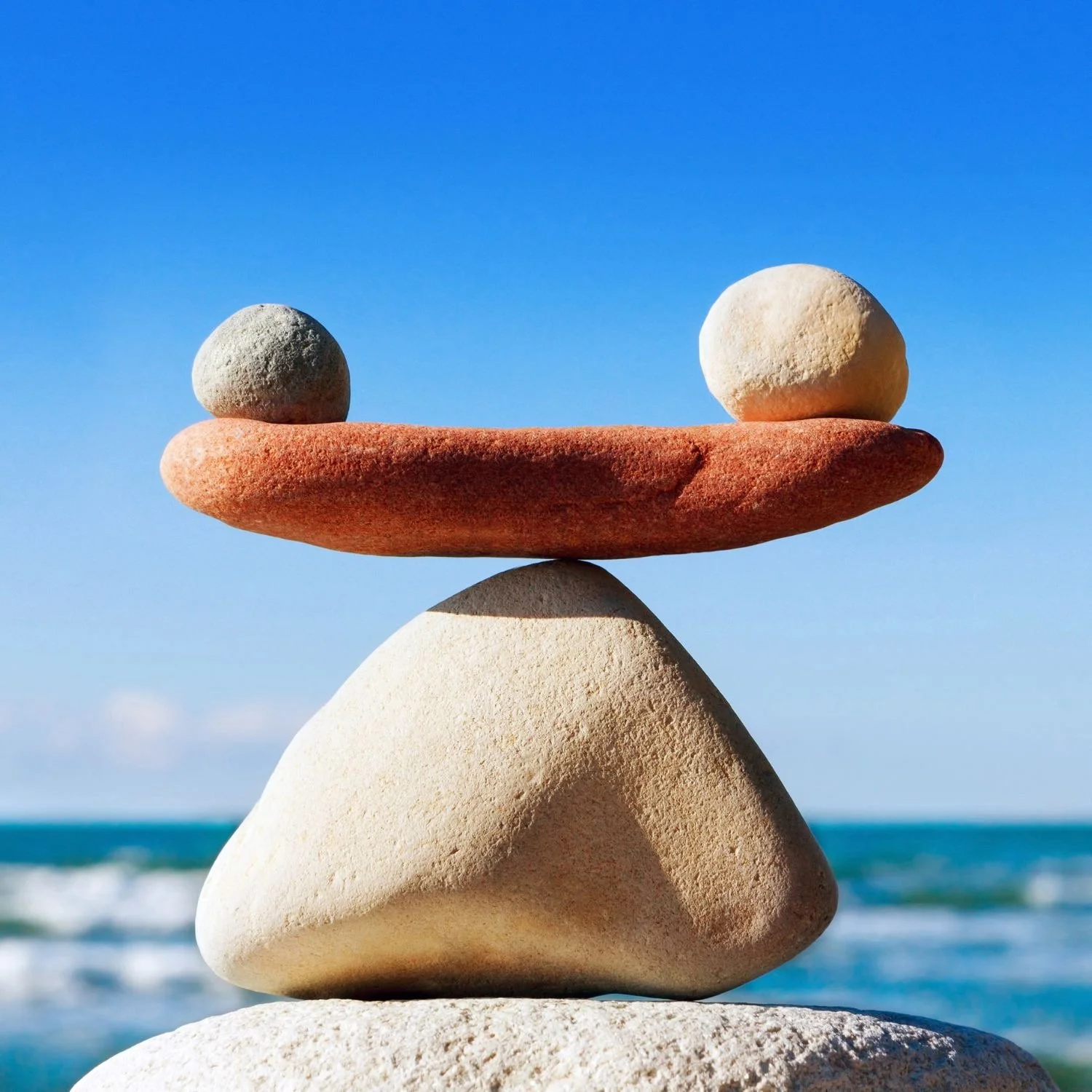 Balanced stones on the beach against a blue sky, symbolizing balance, fulfillment, and mindful growth for high achievers.