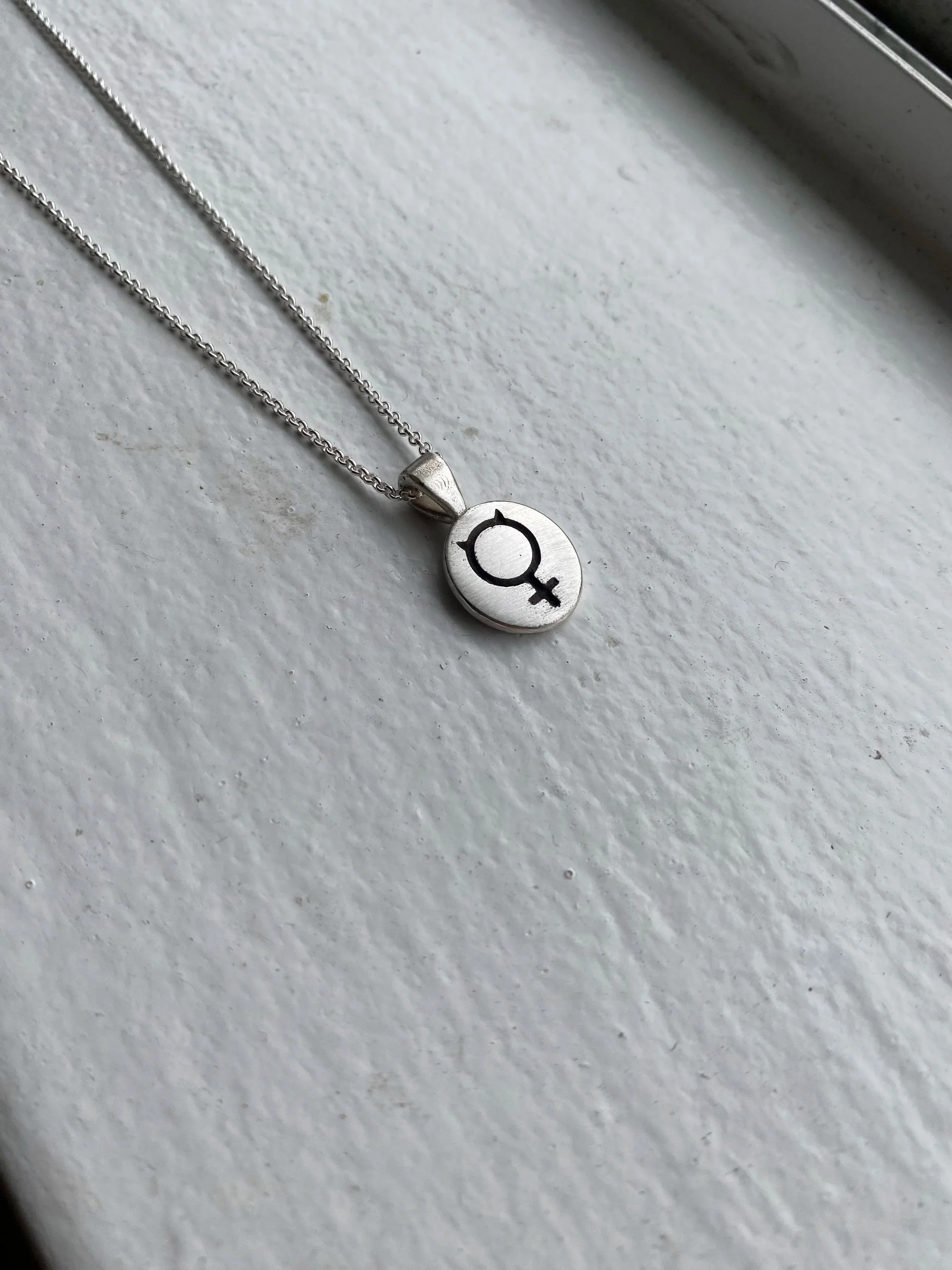 silver pendant with mercury glyph design