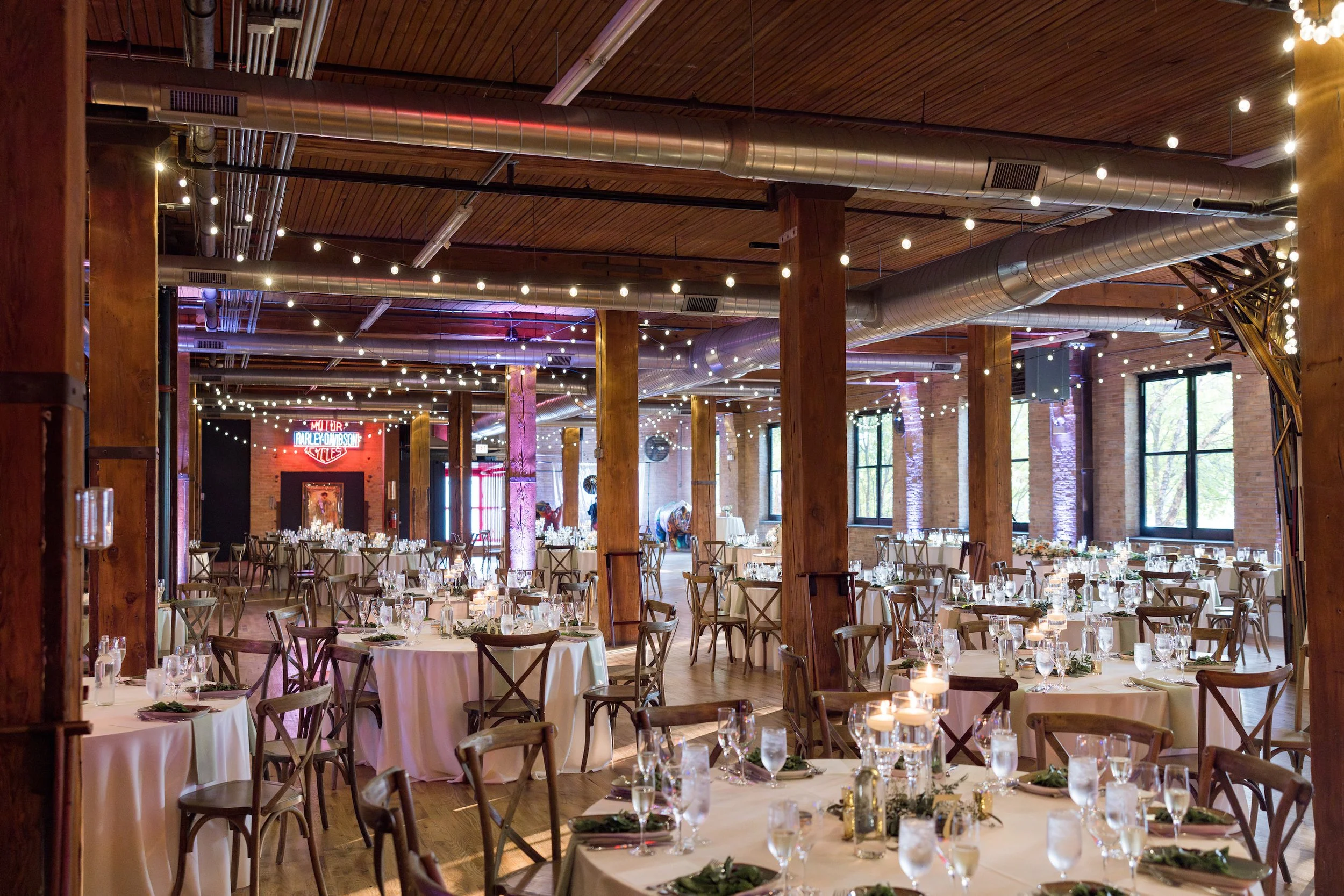 Wedding reception space in urban loft with bistro lights, neon signs, and purple lighting.