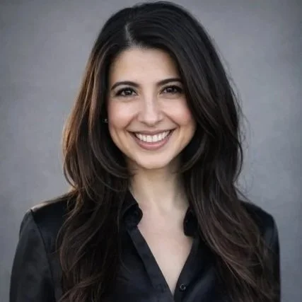 Smiling woman with blonde hair wearing a pink sweater standing beside a wooden fence.