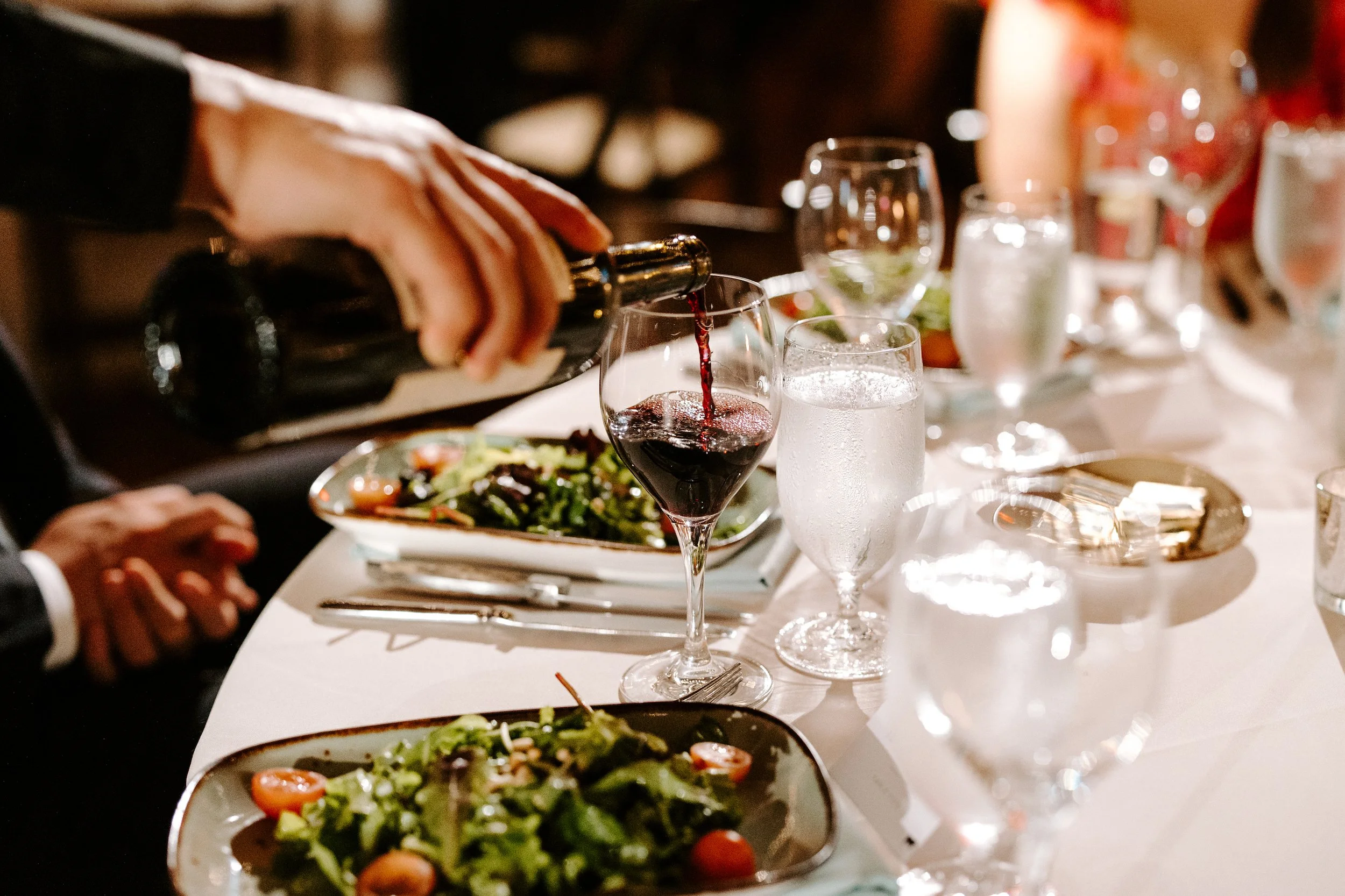 Red wine being poured tableside with guests eating salads. Photo by Kerri Carlquist Photography.