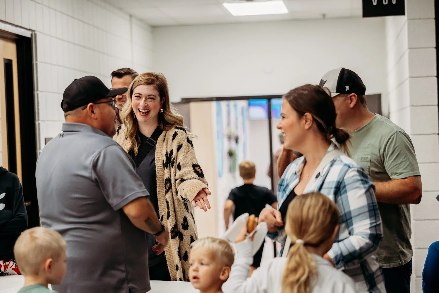 Group of people interacting happily in a hallway, including adults and children, with some people smiling and talking to each other.