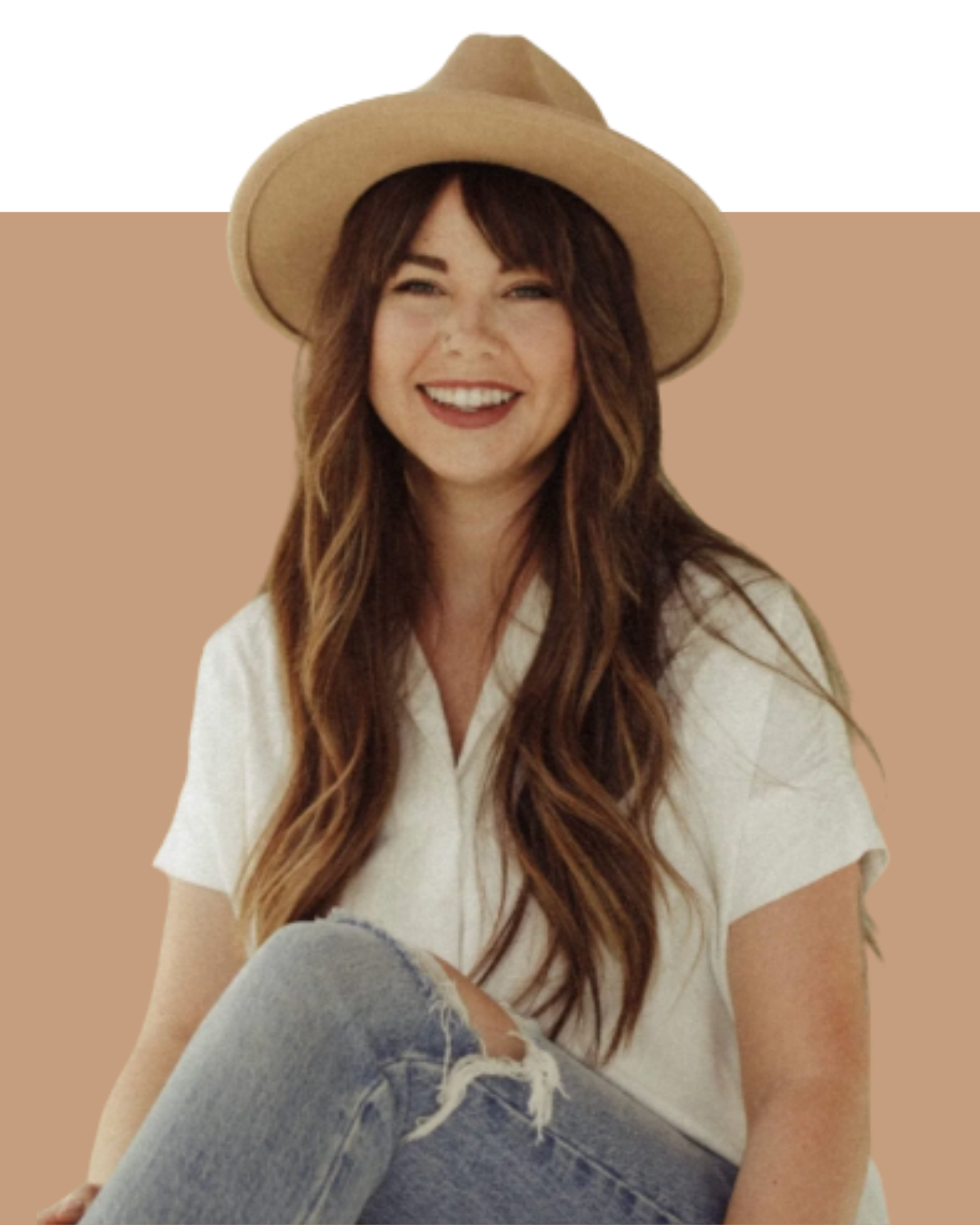 A woman with long brown hair, smiling, wearing a wide-brimmed beige hat and a white shirt, sitting against a two-tone background with tan and purple sections, and wearing blue jeans with a rip in the knee.