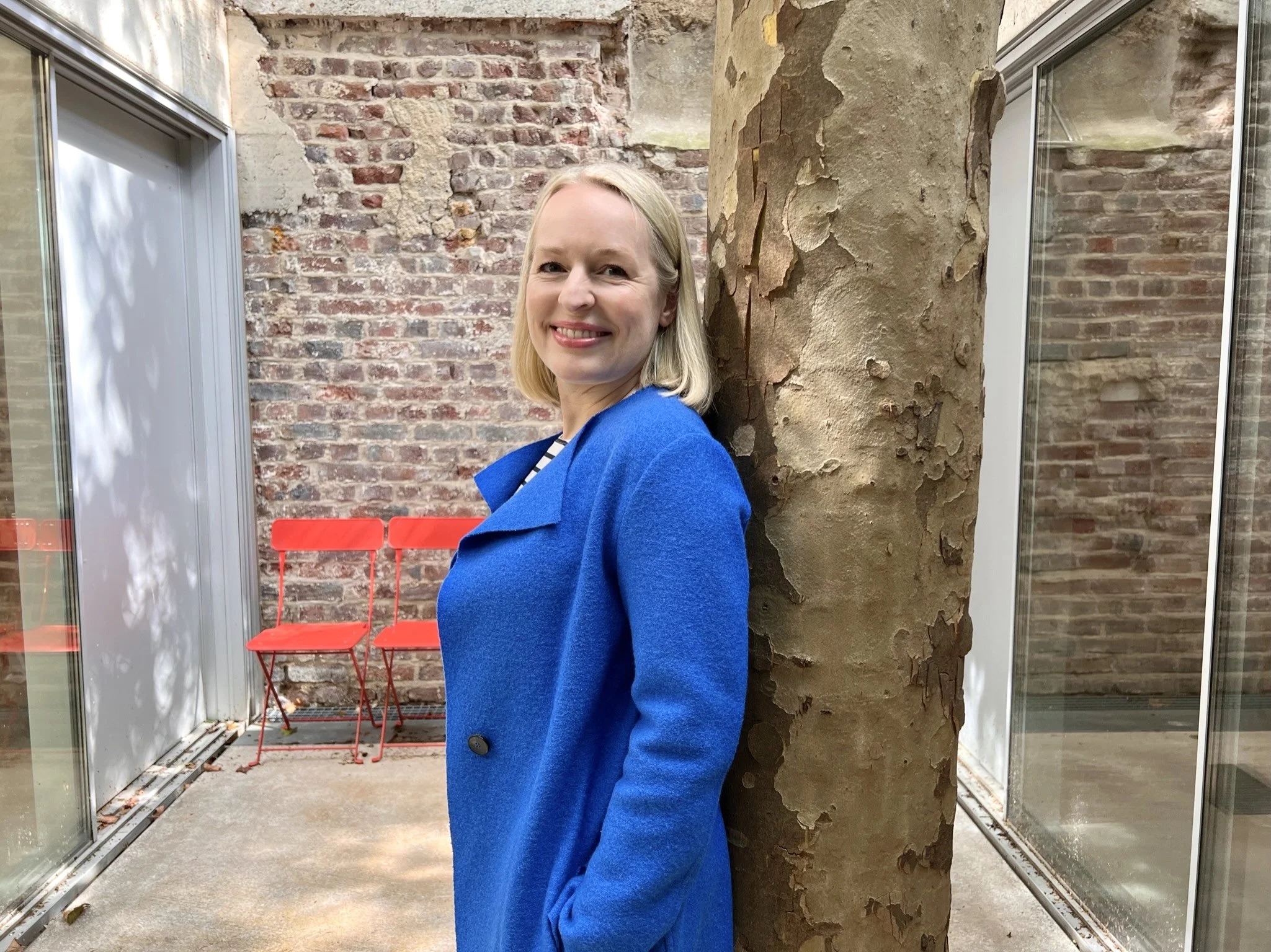Innenarchitektin steht an Baum gelehnt im Atrium des Büros