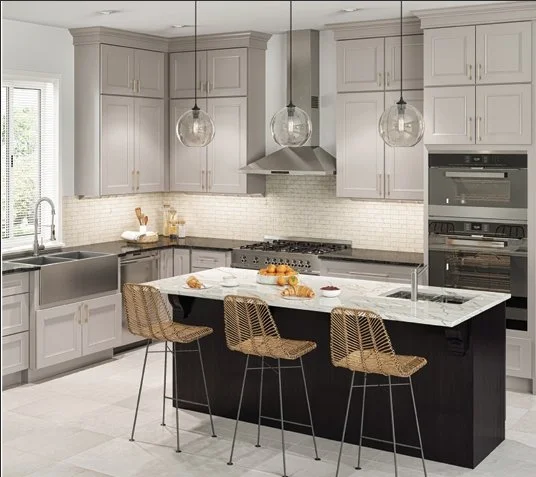 Modern kitchen with light gray cabinets, a central island with a black base and white marble countertop, three wicker barstools, stainless steel appliances, and hanging pendant lights.