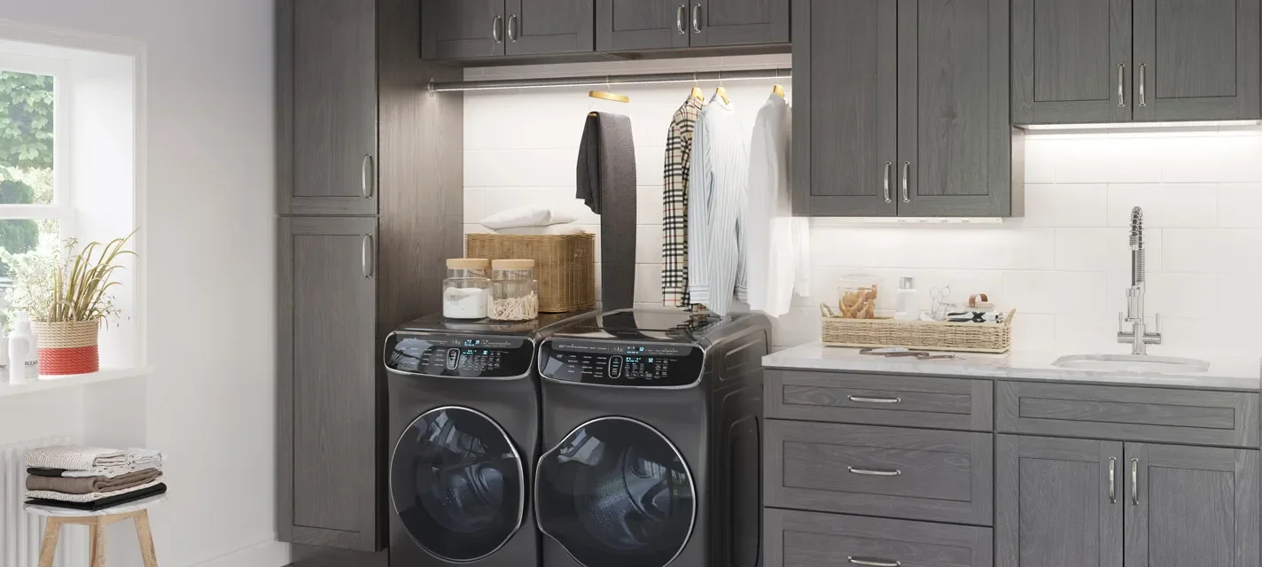 Gray laundry room with washer and dryer, baskets, hanging clothes, and a window with a potted plant.