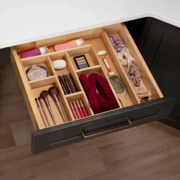 Open drawer with divided compartments containing skincare bottles, makeup brushes, lipsticks, a fabric scrunchie, and hairbrush.
