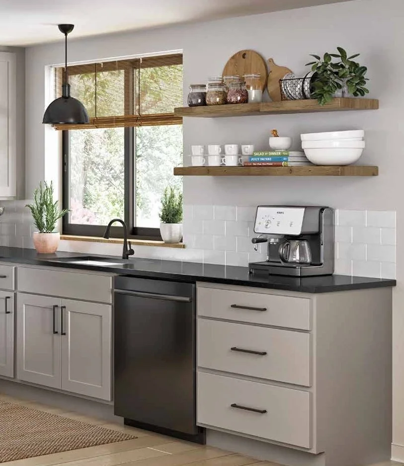 Kitchen with gray cabinets, black countertop, white subway tile backsplash, window with blinds, potted plants, wooden shelves holding jars, bowls, and a cutting board, black coffee maker, and a dishwasher.