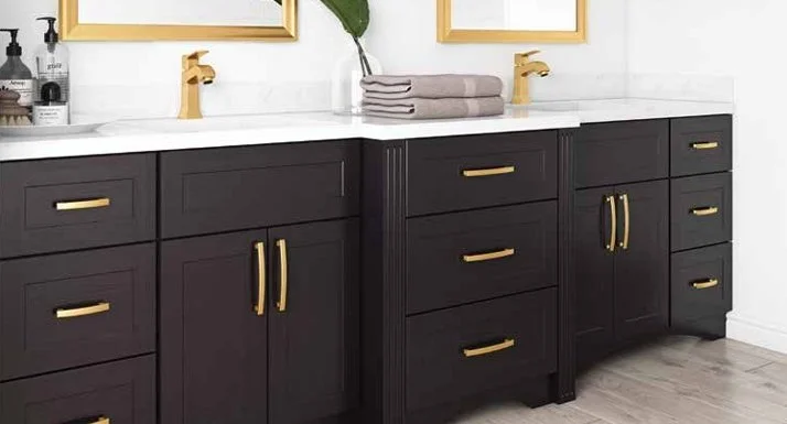 Black bathroom vanity with gold hardware, two sinks, and a white countertop, with folded towels and wall art above.