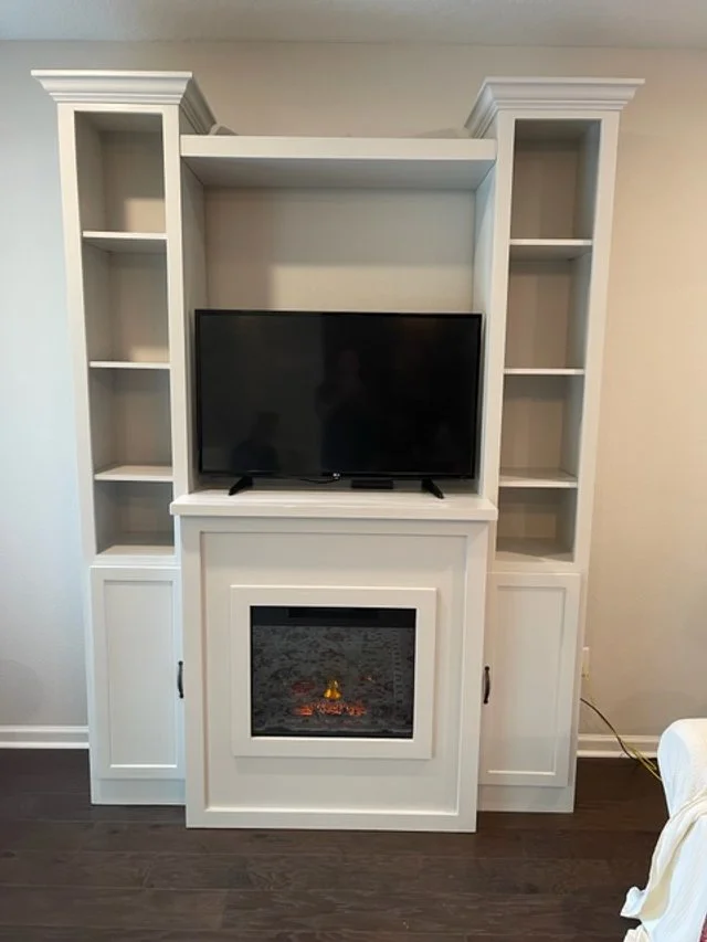 White entertainment center with open shelves, a flat-screen TV, and a built-in electric fireplace in the center.