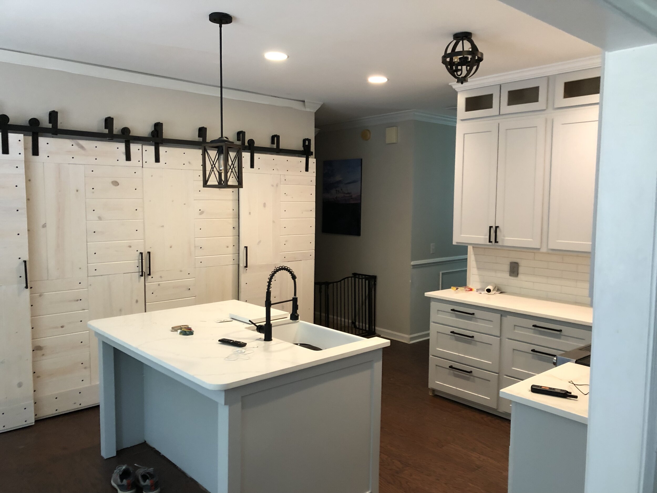 Kitchen with white cabinets and an island, barn door on sliding track, black hardware, and a decorative black pendant light.