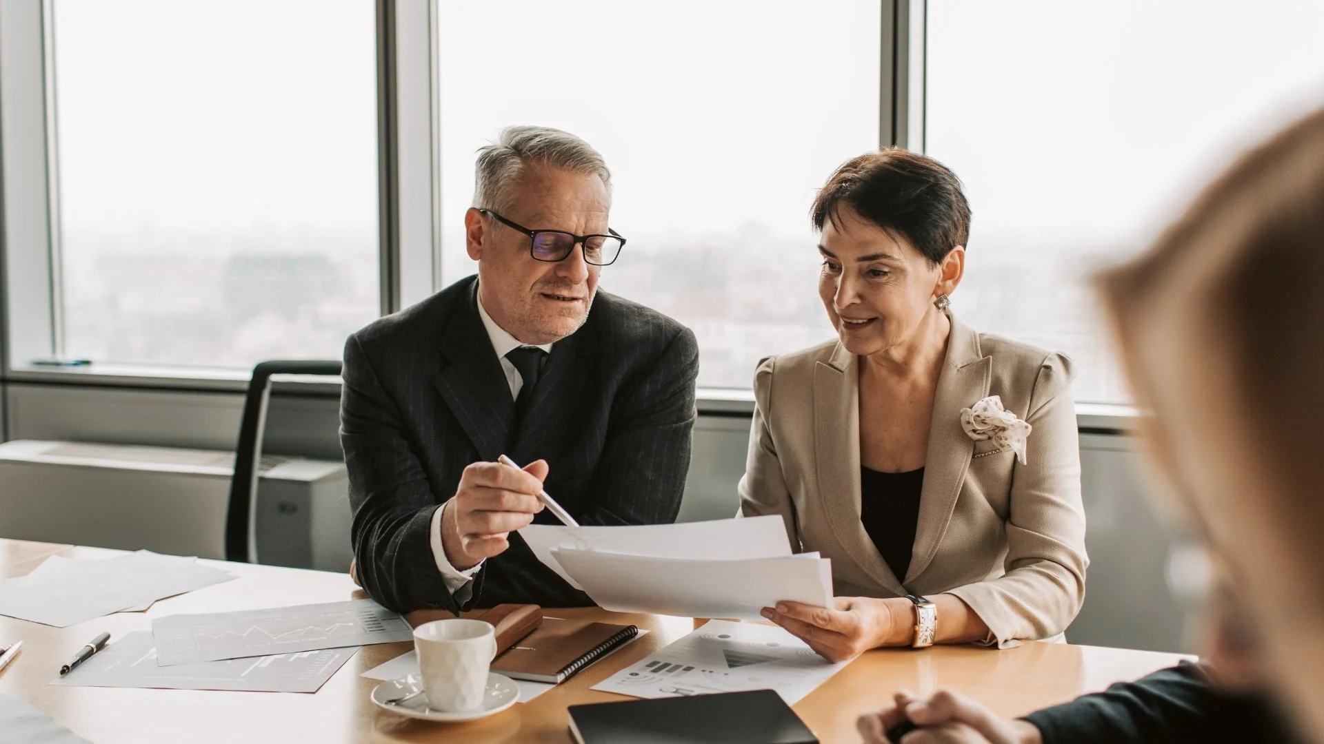 A professional couple in a high-end office discussing a financial chart on a tablet with an advisor.