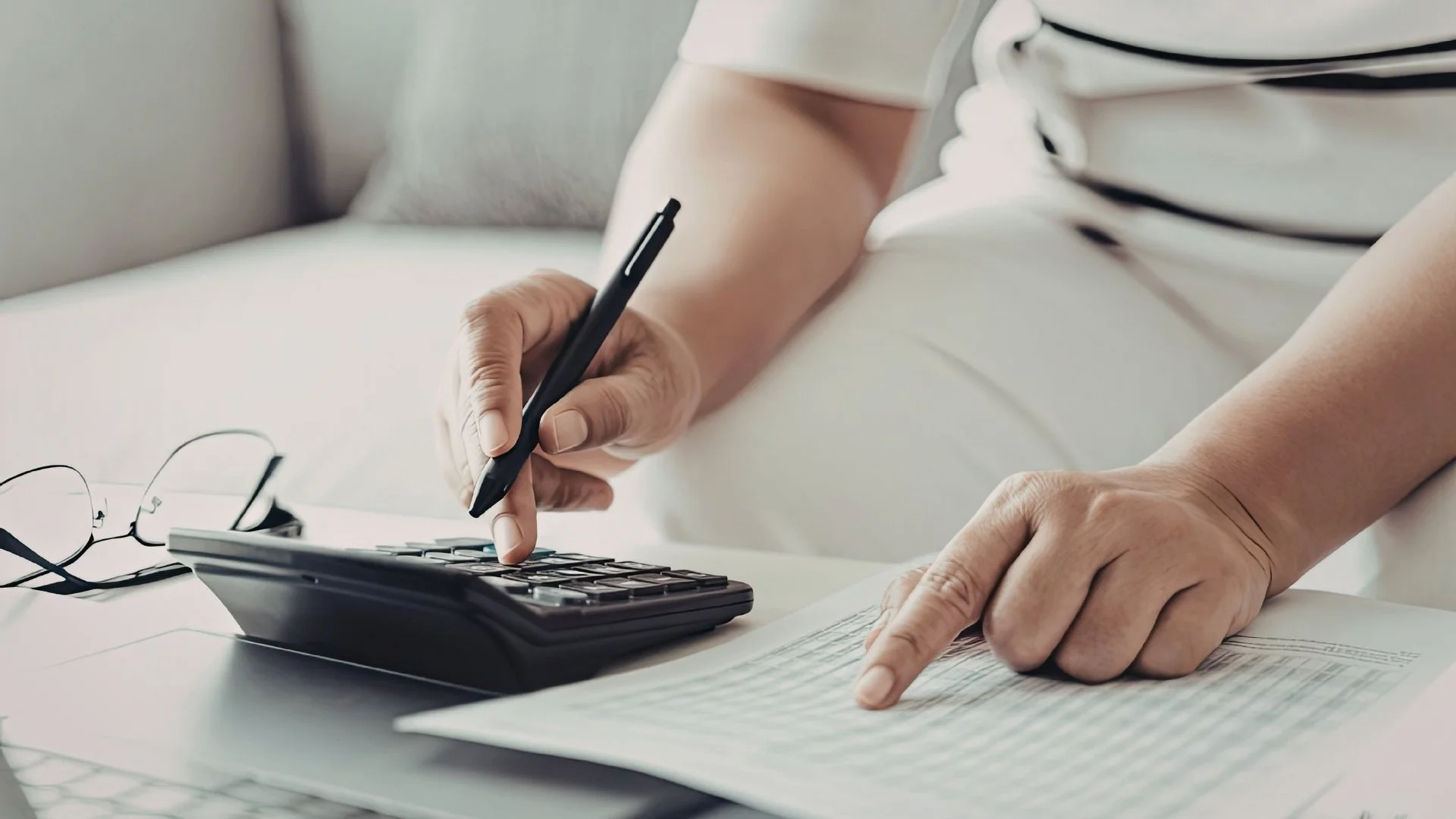 A minimalist workspace featuring a high-end calculator, a leather ledger, and a glass of water