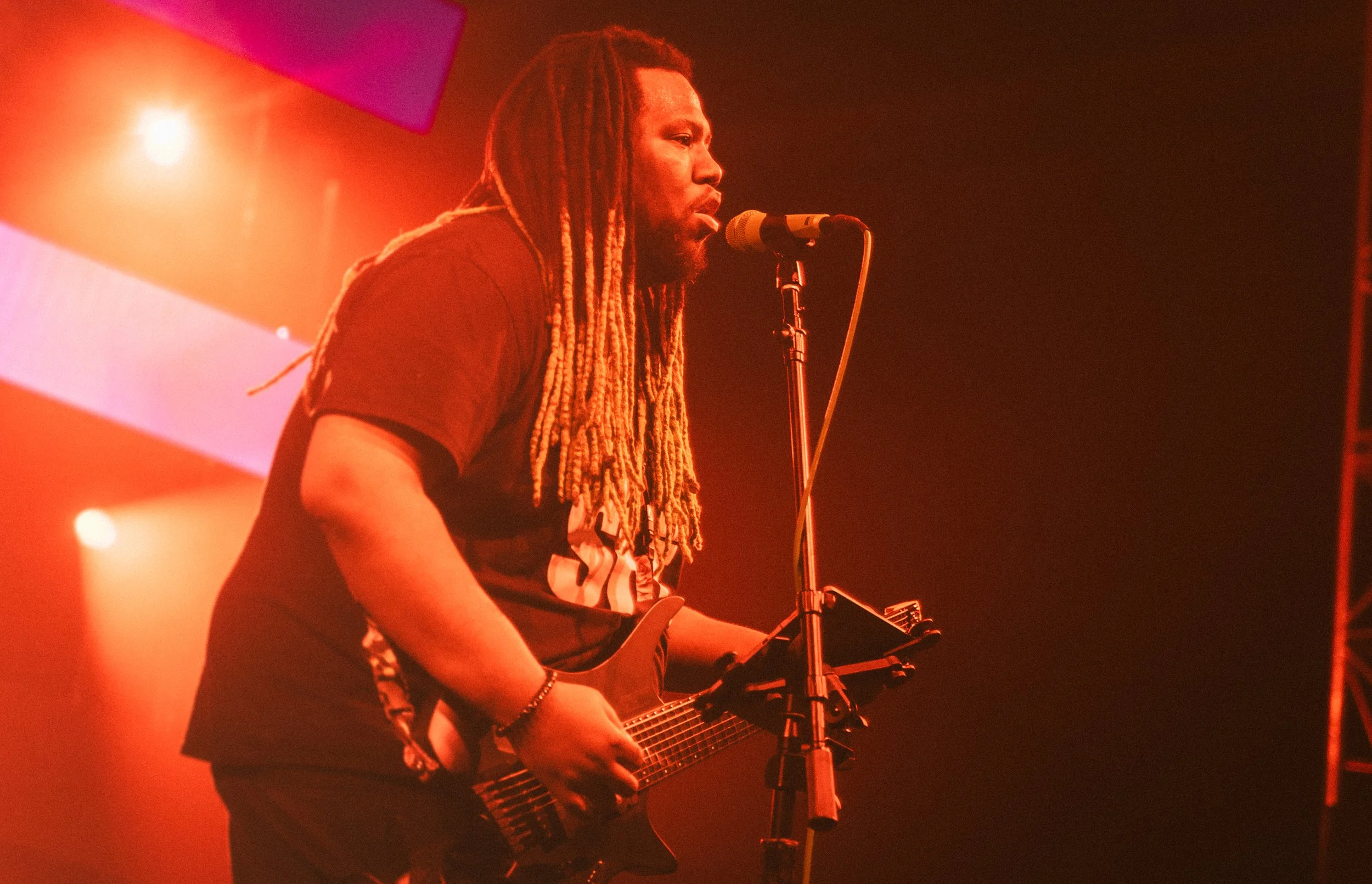 Musician and Composer Tre Watson playing an electric guitar and singing into a microphone on stage, with orange stage lighting.