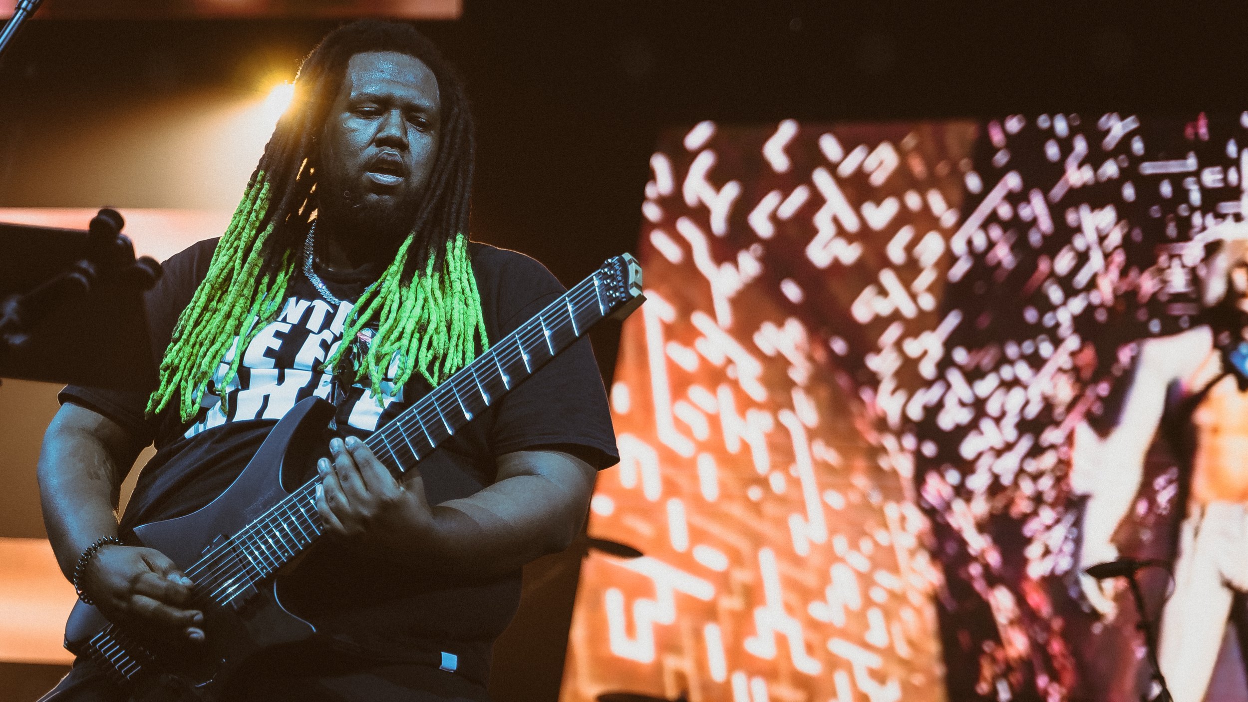 Musician and Composer Tre Watson  playing an electric guitar on stage with a colorful background.