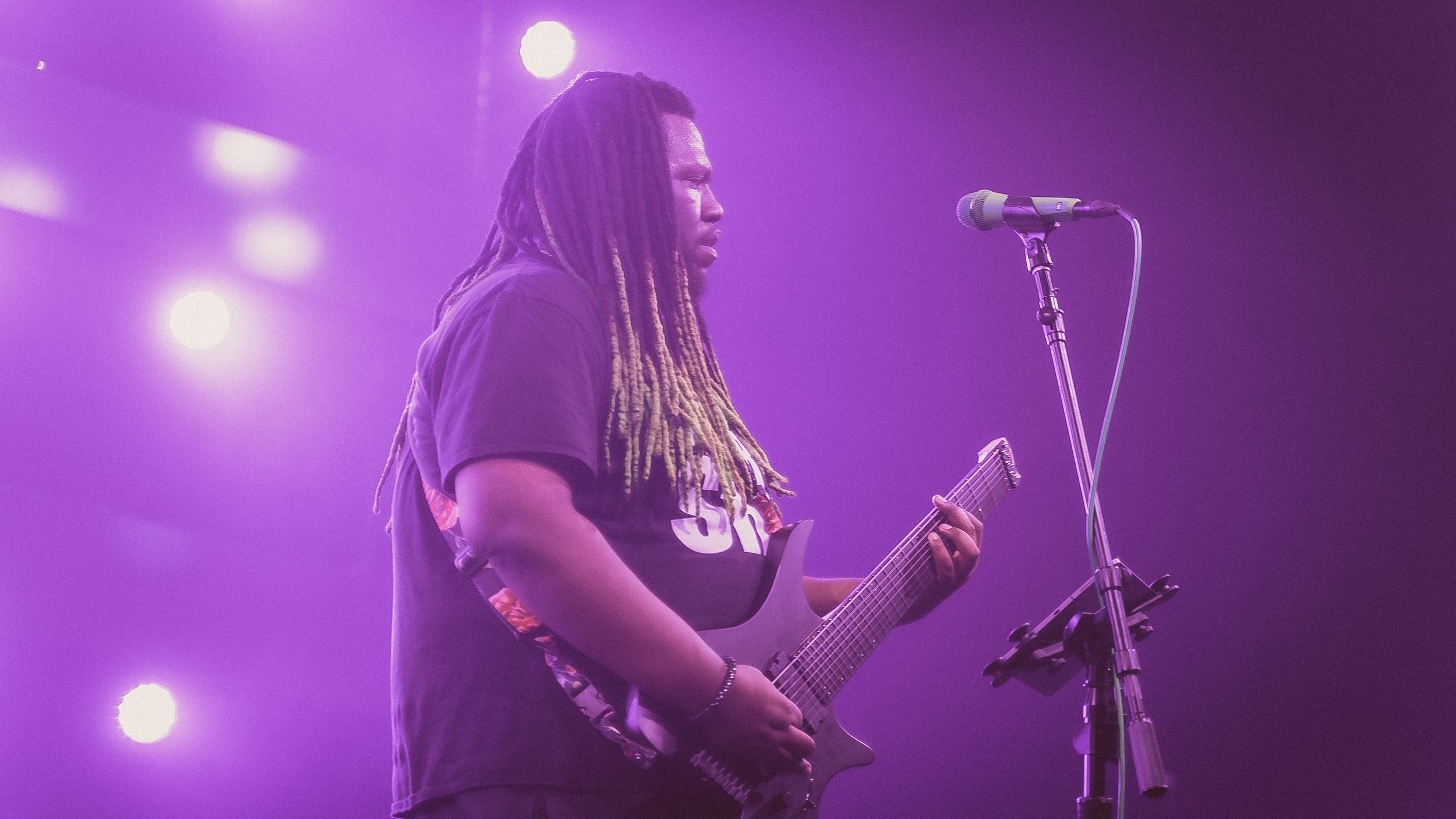 Musician and Composer Tre Watson  playing an electric guitar on stage under purple lighting.
