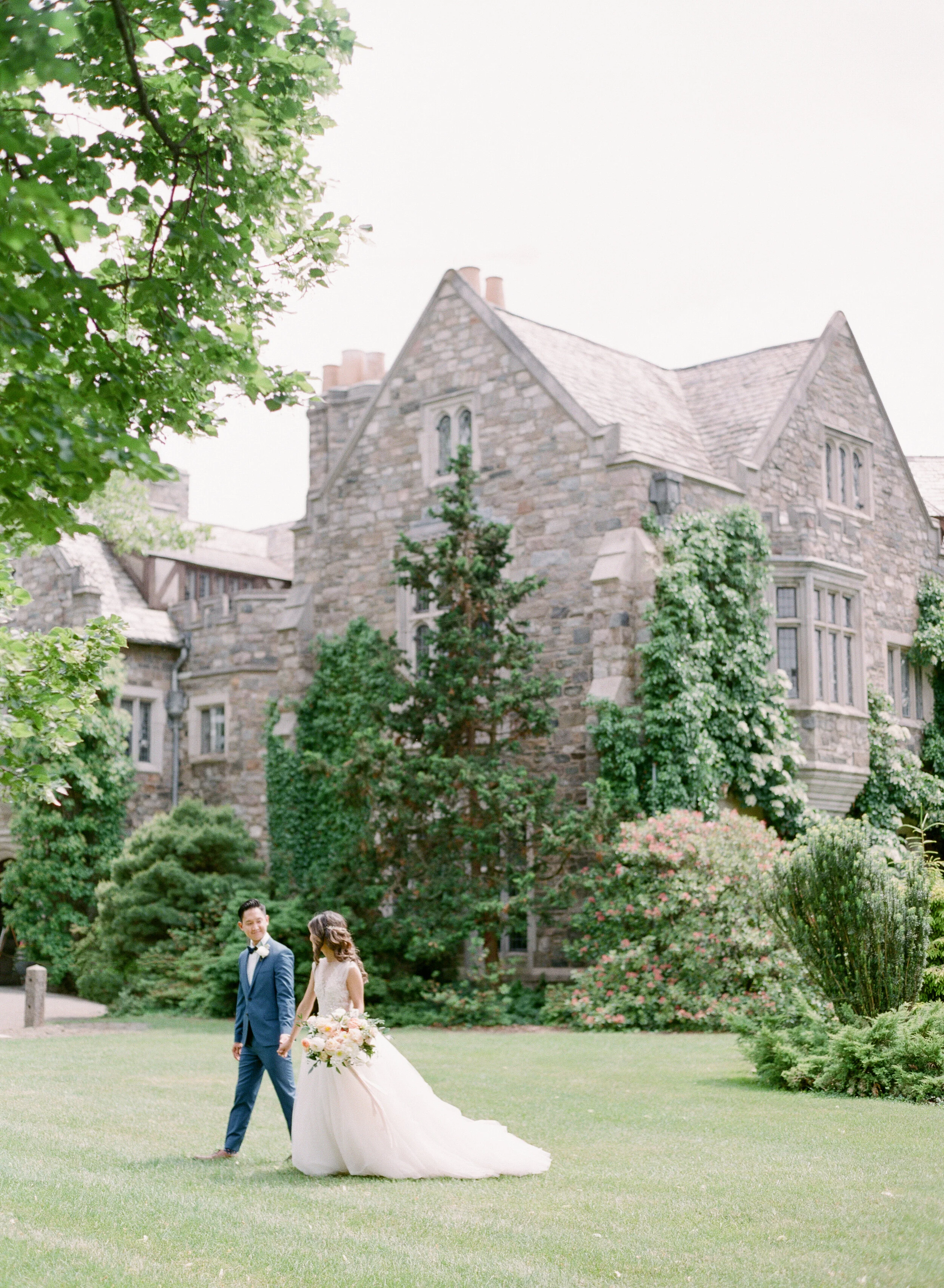 Skylands Manor destination wedding bride & groom walking with organic wedding bouquet and tulle wedding gown paired with blue suit