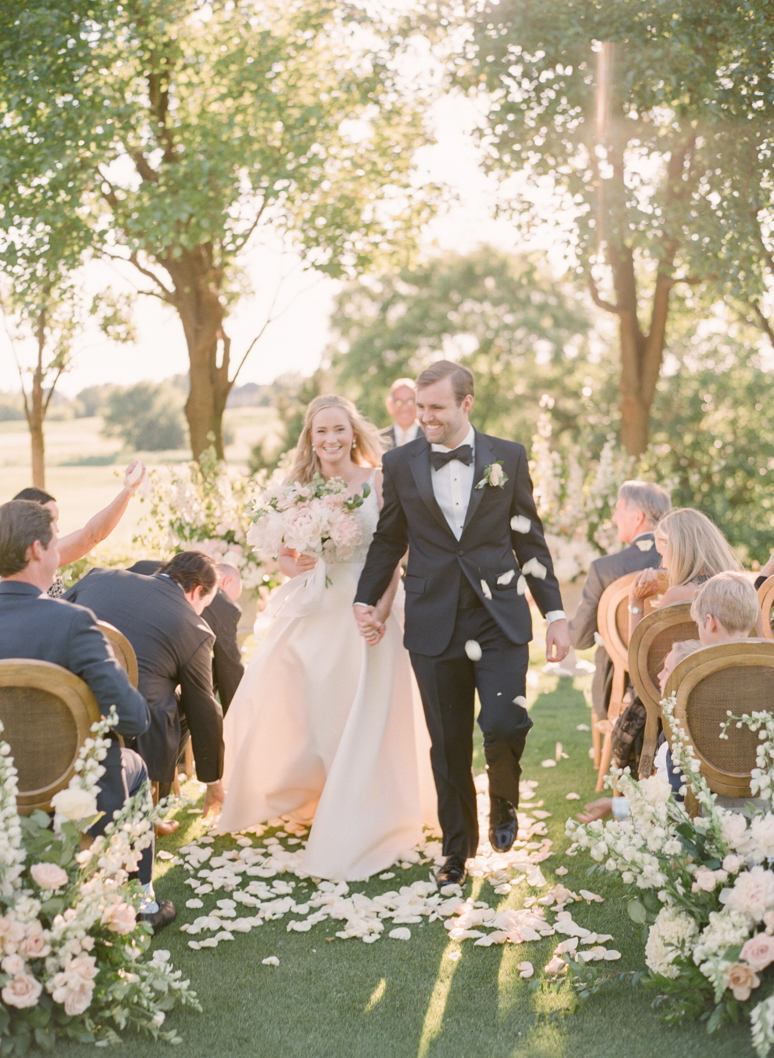 Gaillardia wedding couple holding hands with organic florals and rose petal toss during the recessional - Oklahoma City Wedding Photographer