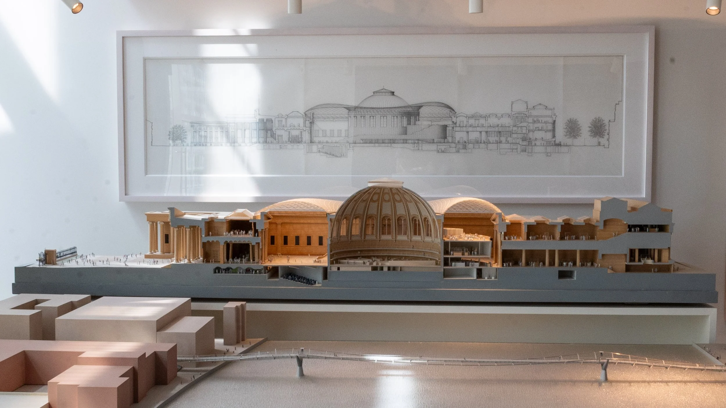 Architectural model of a building with a large dome and classical columns, displayed on a table in front of a framed architectural drawing.