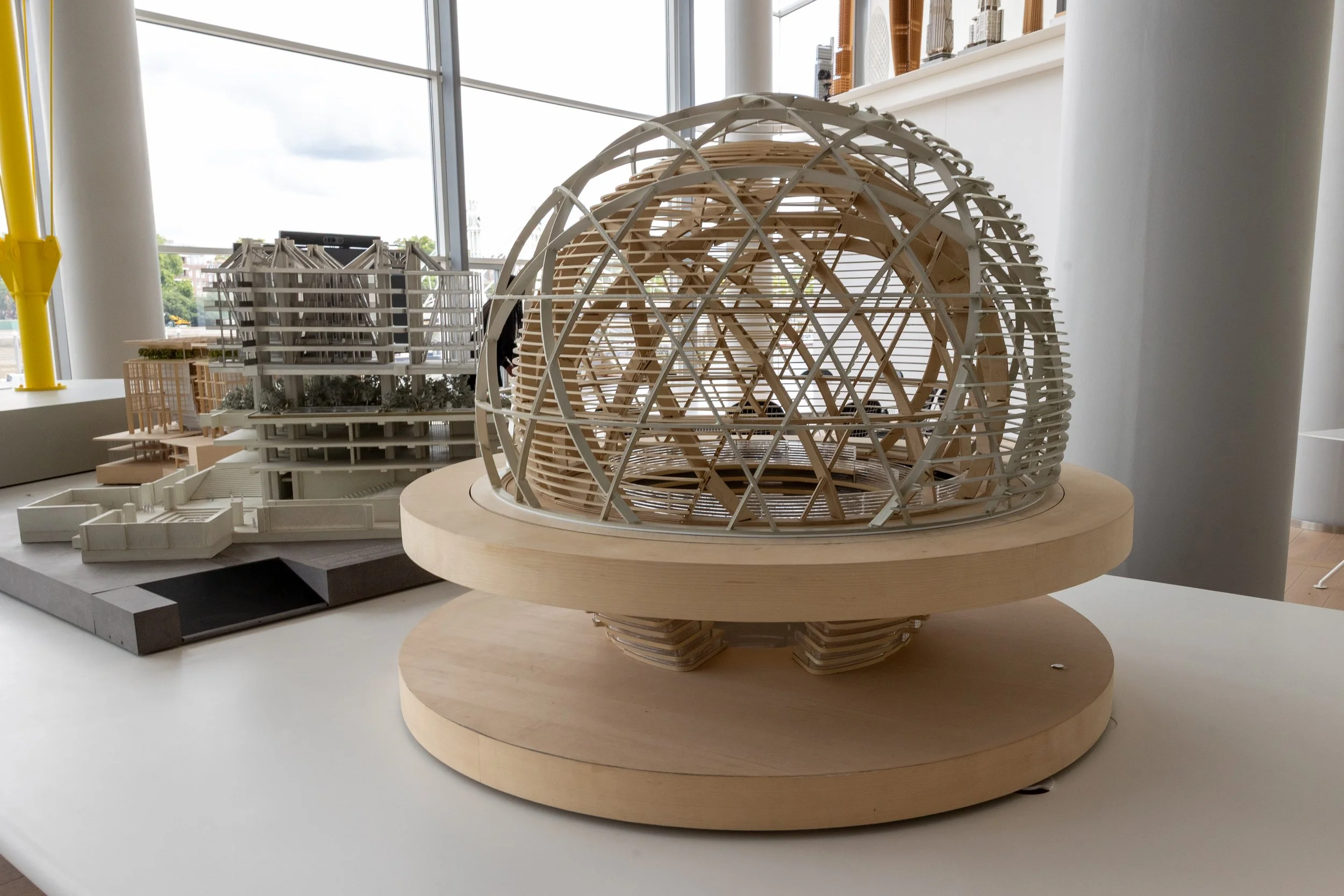 Architectural models of futuristic building designs displayed on a table in a modern interior with large windows.