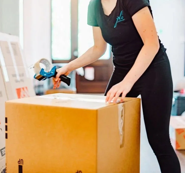 Person sealing a cardboard box with packing tape using a tape dispenser.