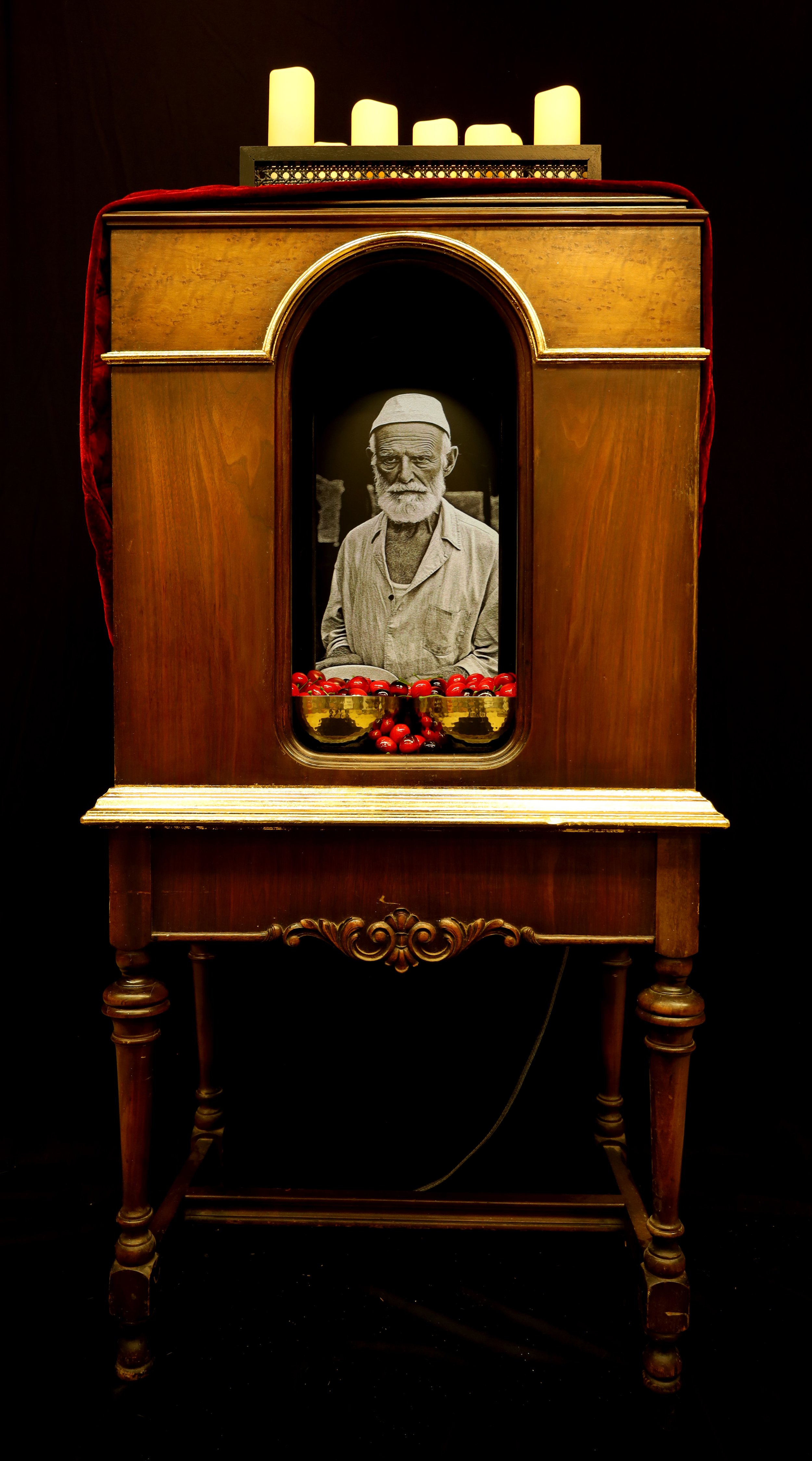  History of the Seeder Nation , 2024, faux cherries, LED candles, monitor, repurposed cabinet, metal bowls, cloth, wood