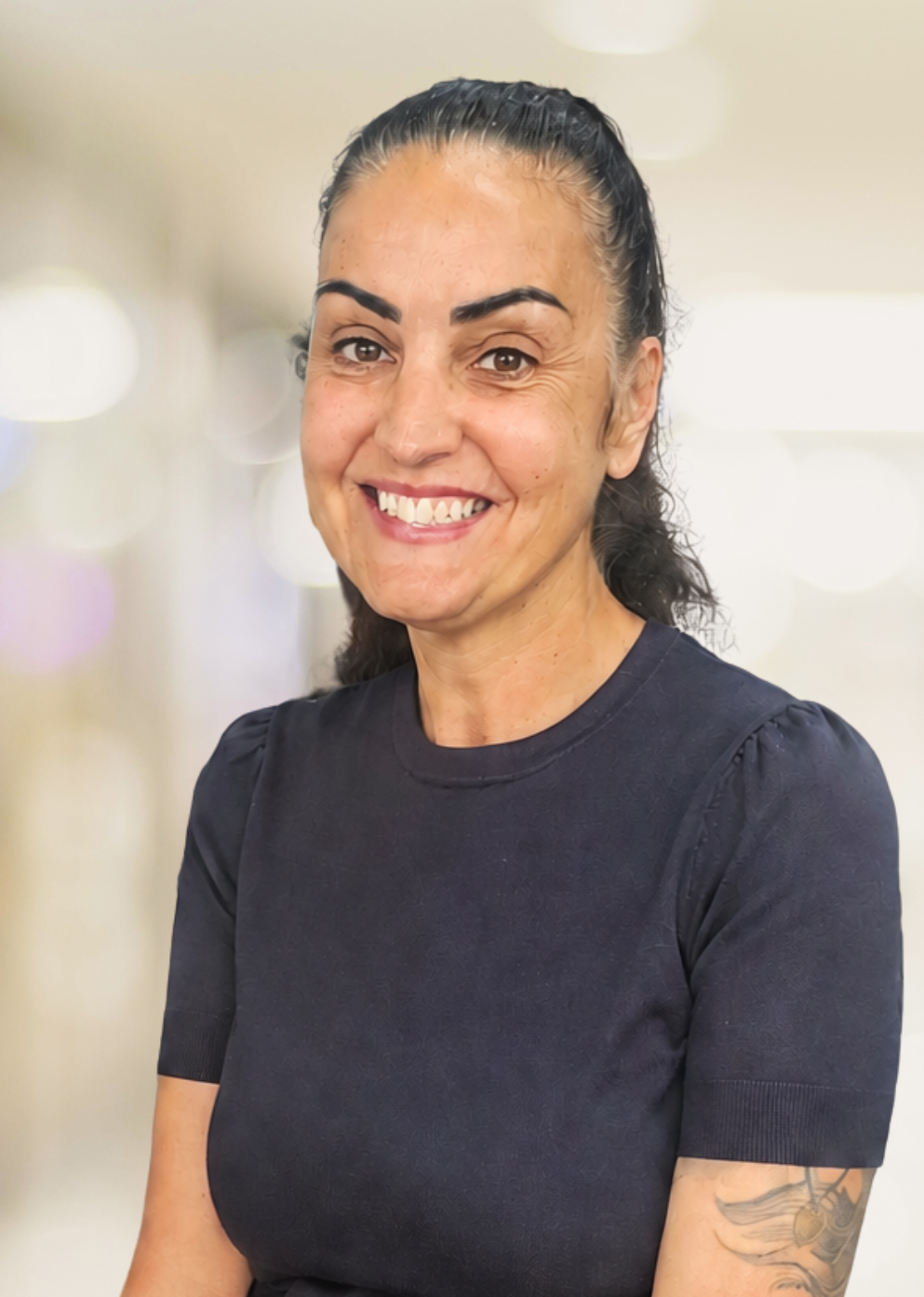 Smiling woman with dark hair in a ponytail wearing a navy top, posed for a portrait