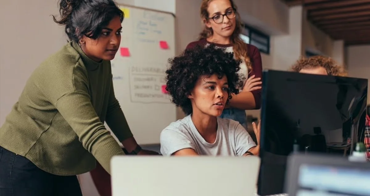 Four women working together around a computer in an office.