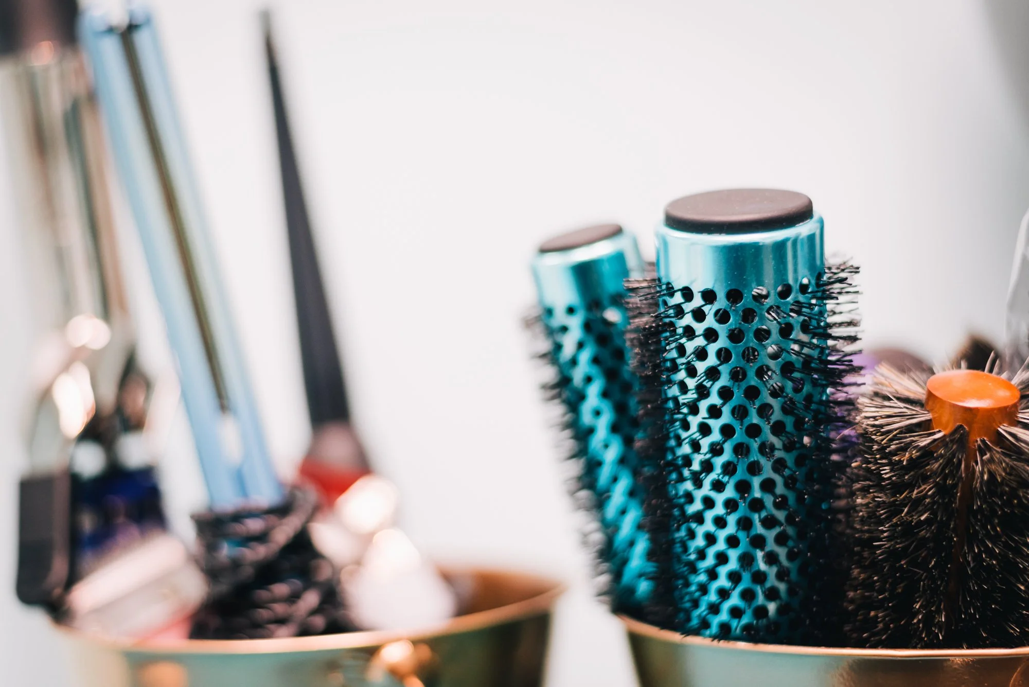 two teal and black round brushes are in a gold bucket