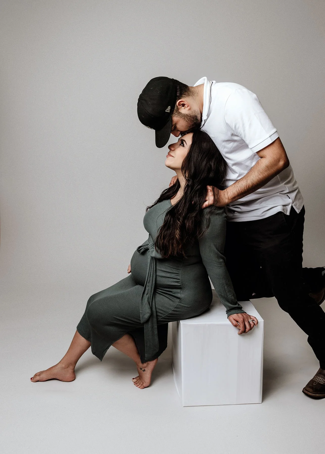 Daddy leaning over mama, kissing forehead, baby bump visible